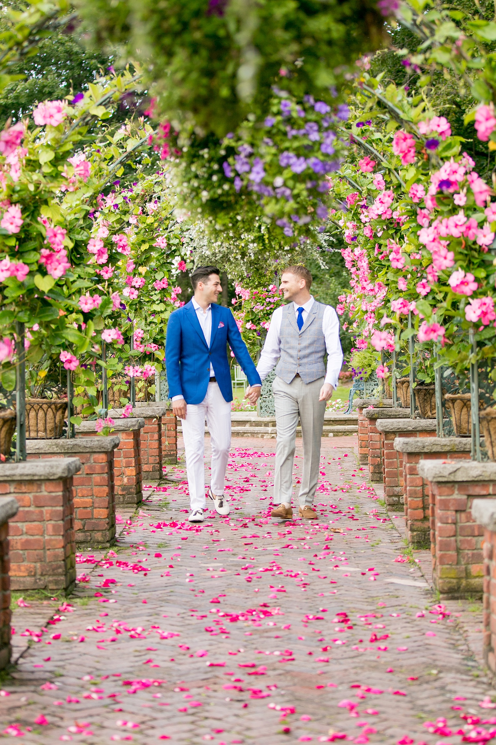 Mikkel Paige Photography photos of a gay wedding at The Manor in West Orange, NJ. The grooms walk to their outdoor summer ceremony on a rose petal carpet under live arches and greenery.