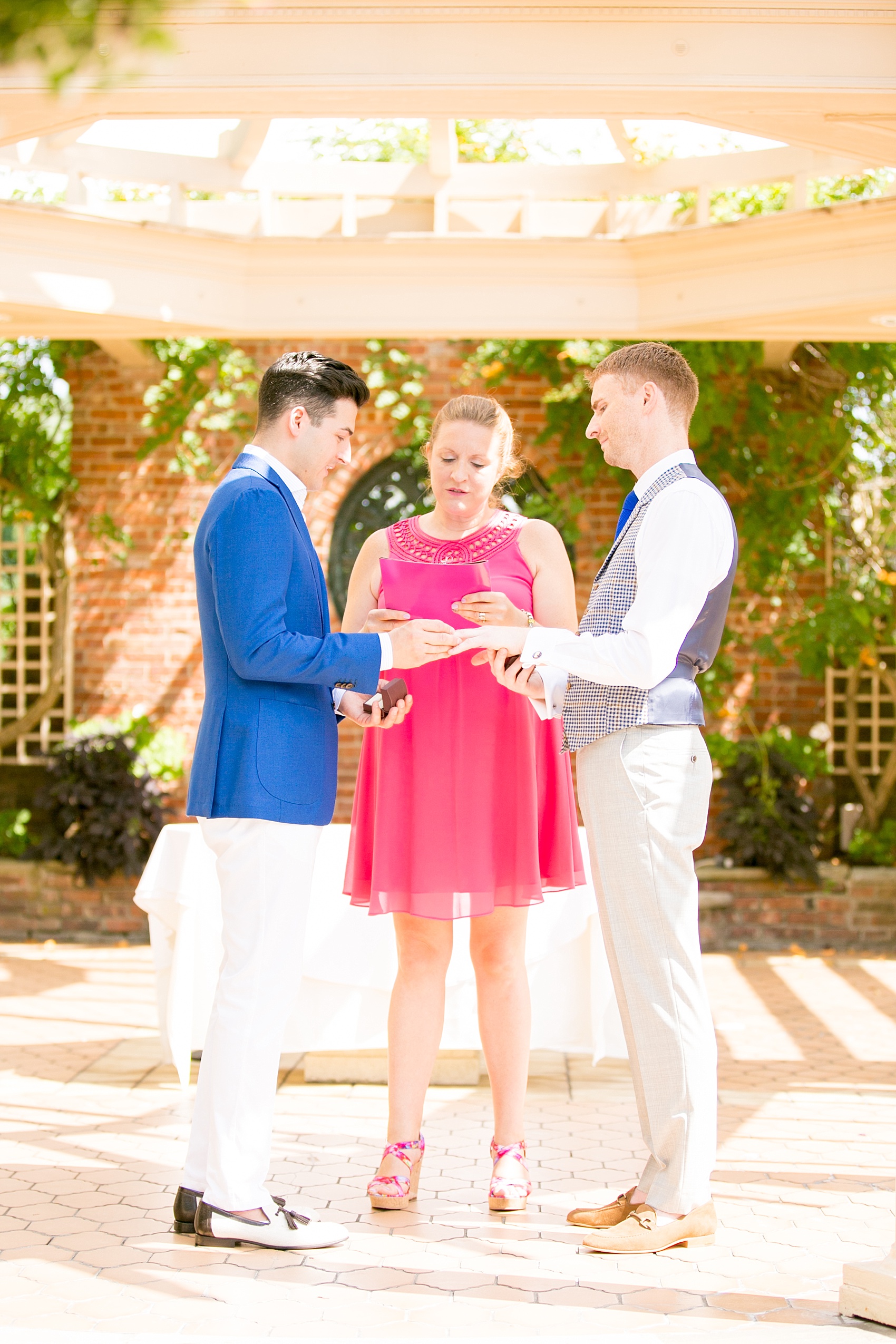 Mikkel Paige Photography photos of a gay wedding at The Manor in West Orange, NJ. Image of grooms exchanging rings during their outdoor ceremony.