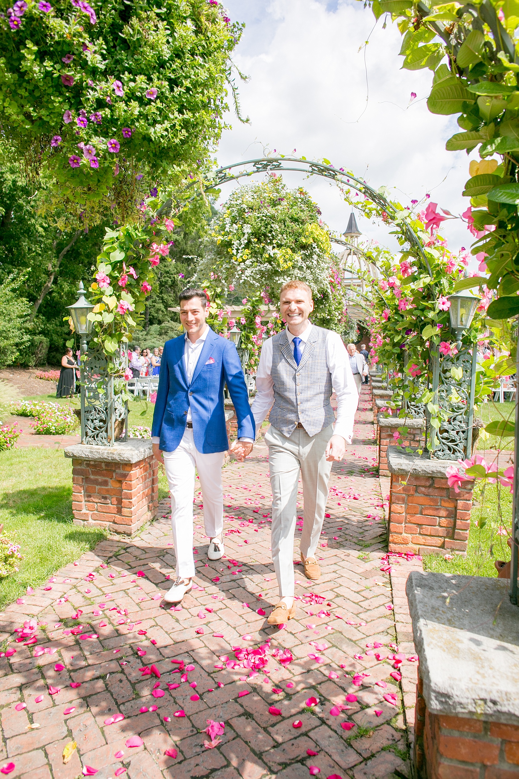 Mikkel Paige Photography photos of a gay wedding at The Manor in West Orange, NJ. The grooms walk from their outdoor summer ceremony on a rose petal carpet under live arches and greenery.