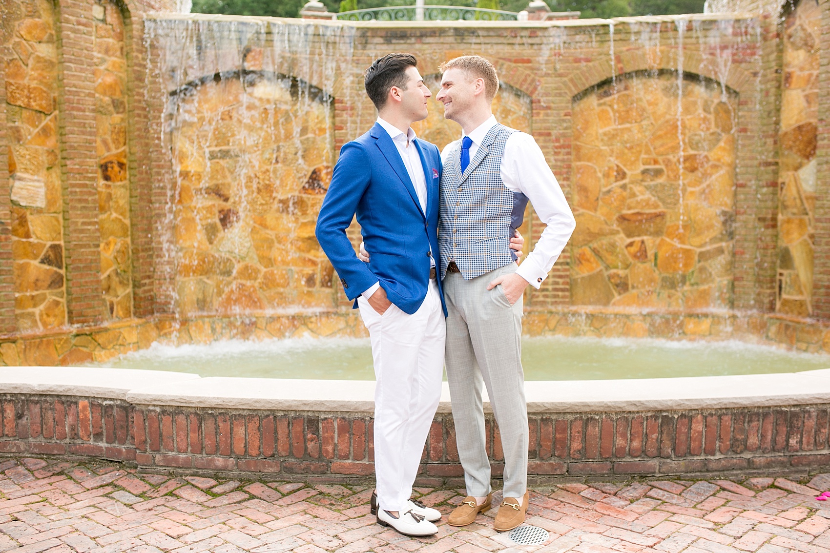 Mikkel Paige Photography photos of a summer, daytime gay wedding. An image of the grooms in a vest and blue suit in front of a picturesque fountain at The Manor, in West Orange New Jersey.