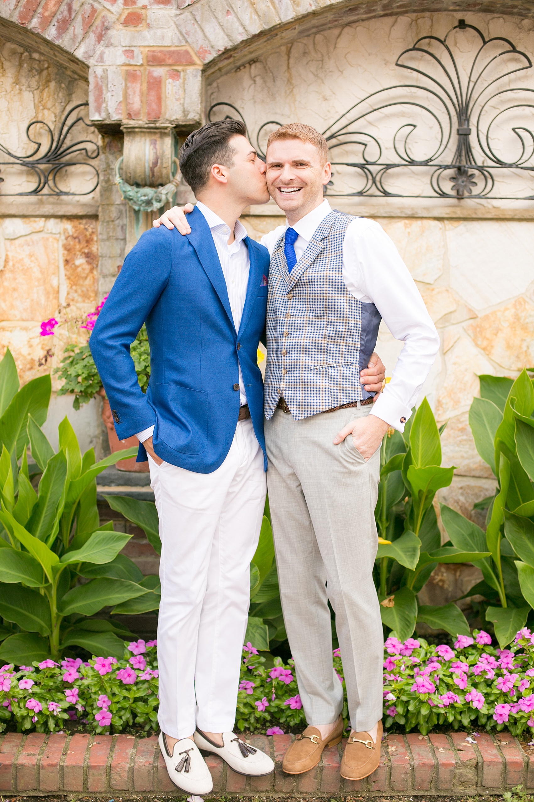 Mikkel Paige Photography photos of a summer, daytime gay wedding. An image of the grooms in a vest and blue suit in front of picturesque landscaping at The Manor, in West Orange New Jersey.