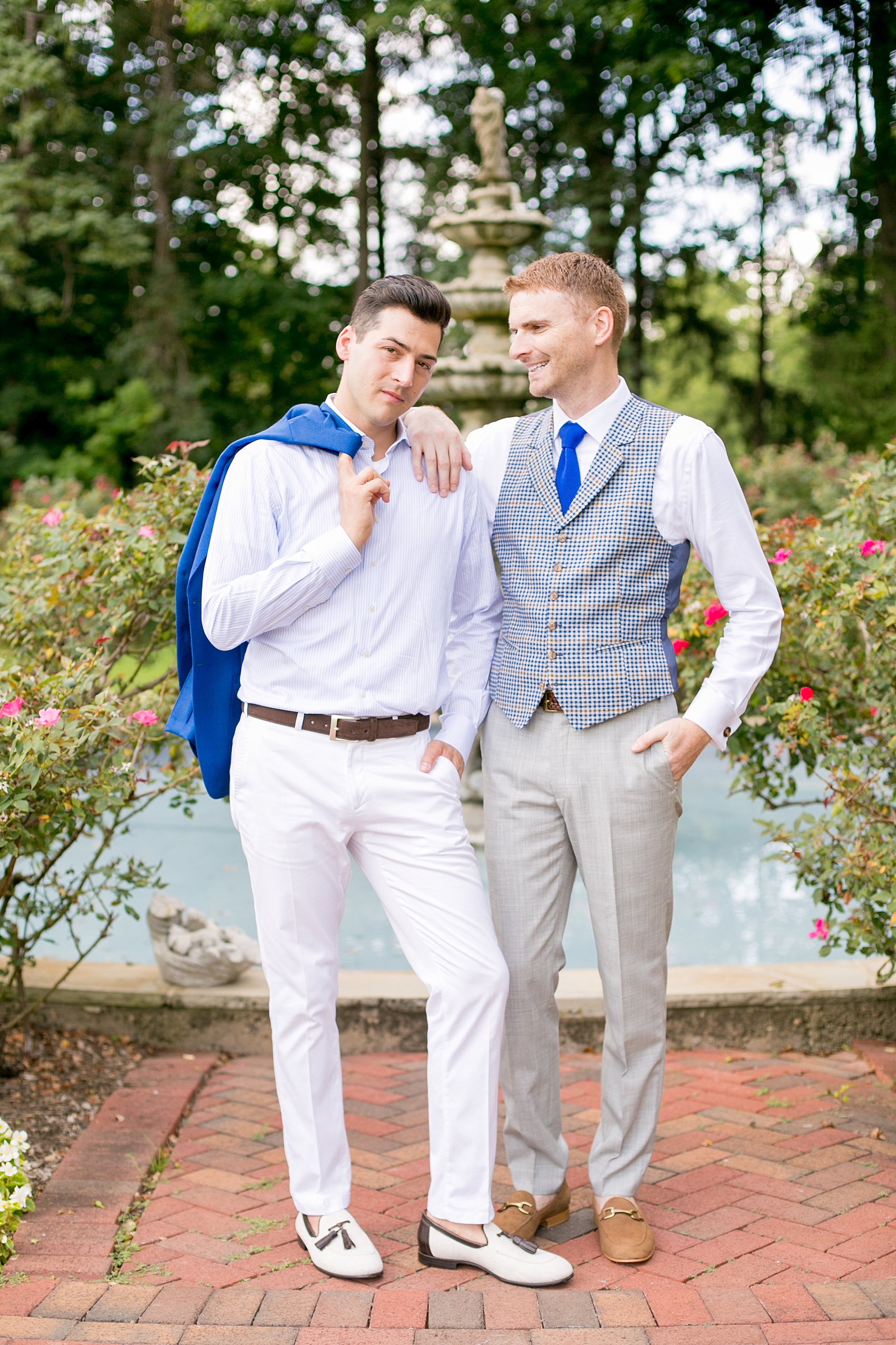 Mikkel Paige Photography photos of a summer, daytime gay wedding. An image of the grooms in a vest and blue suit in front of a fountain and pool, with rose bushes at The Manor, in West Orange New Jersey.