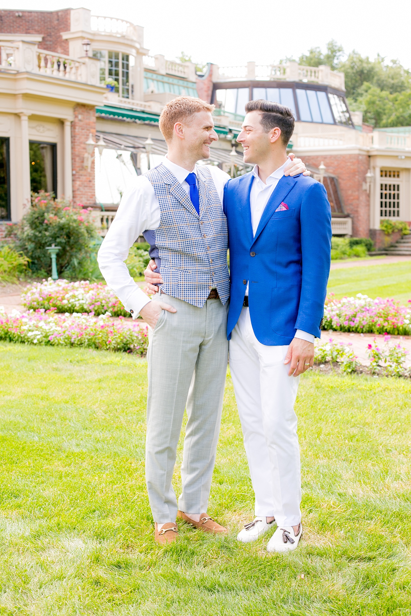 Mikkel Paige Photography photos of a summer, daytime gay wedding. An image of the grooms in a vest and blue suit in front of picturesque landscaping at The Manor, in West Orange New Jersey.