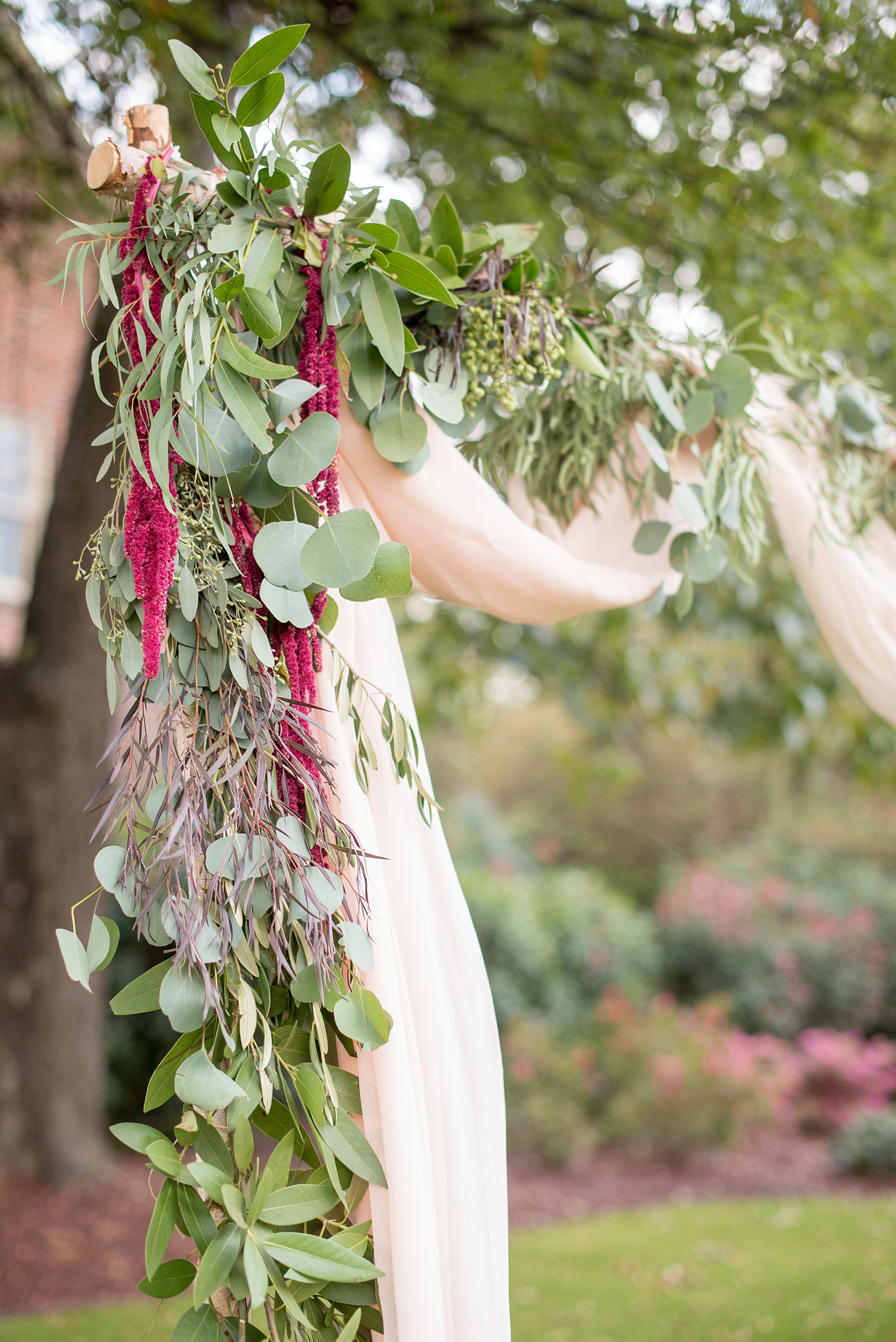 Mikkel Paige Photography photos from a Merrimon-Wynne House wedding in Raleigh. An outdoor ceremony setup with floral arbor with silver dollar eucalyptus and draped fabric for a same-sex wedding.