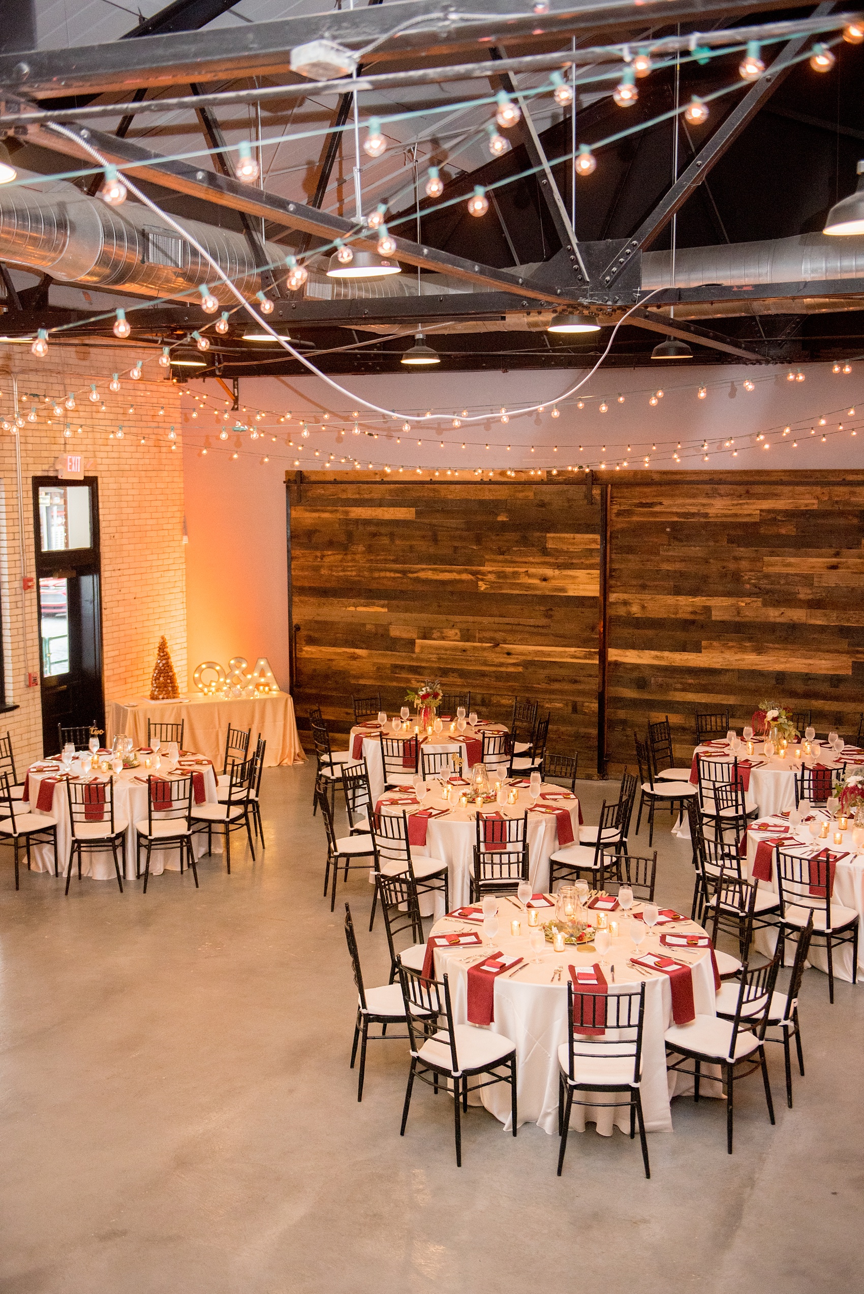 Mikkel Paige Photography photos from a wedding at 214 Martin Street in downtown Raleigh with burgundy and white fall flowers and bistro market lights. Gold painted script wood words served as table numbers.