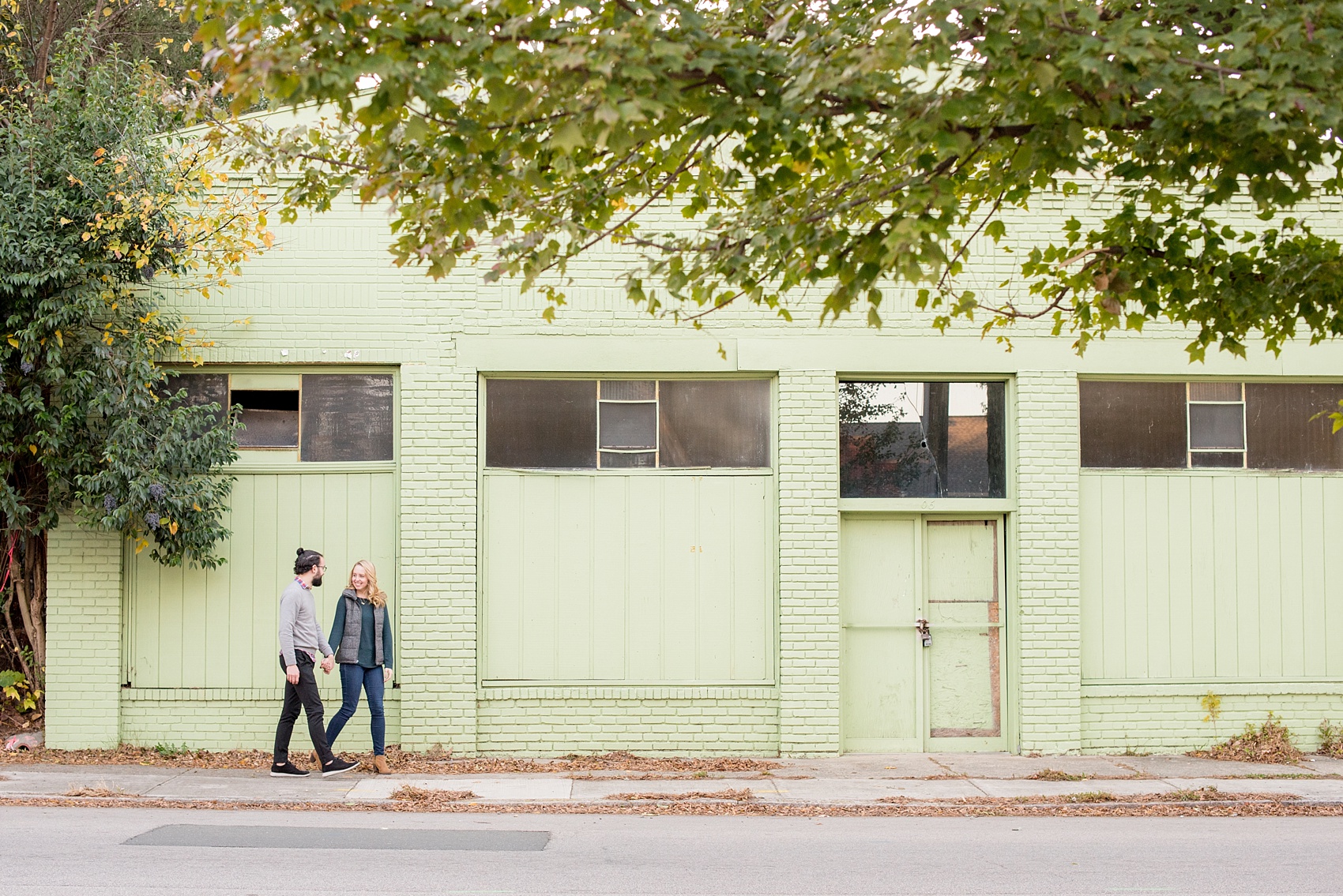 Mikkel Paige Photography photos of a downtown Durham engagement session. A picture of the couple walking in front of a mint green aging building.