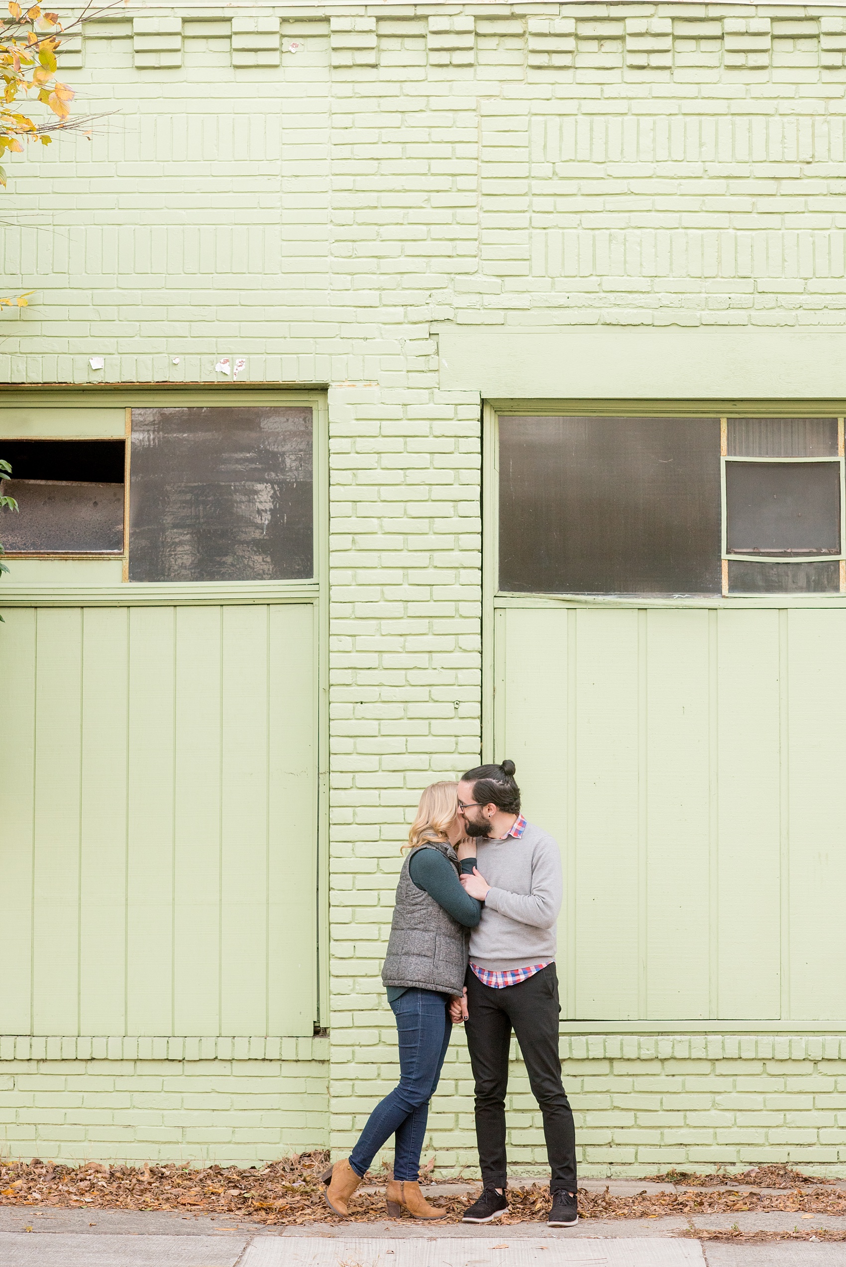Mikkel Paige Photography photos of a downtown Durham engagement session. A picture of the couple walking in front of a mint green aging building.