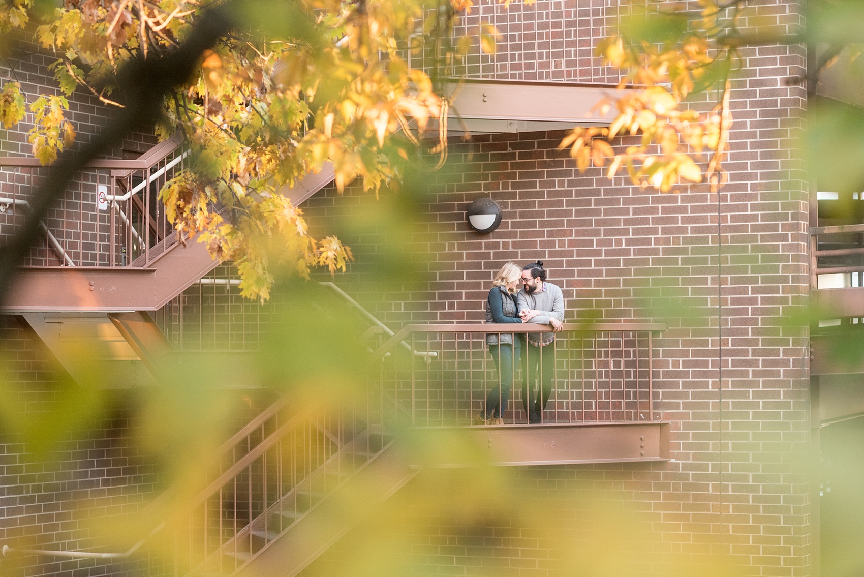 Mikkel Paige Photography photos of a downtown Durham engagement session. A picture of the bride and groom on a balcony peeking through amongst fall leaves.