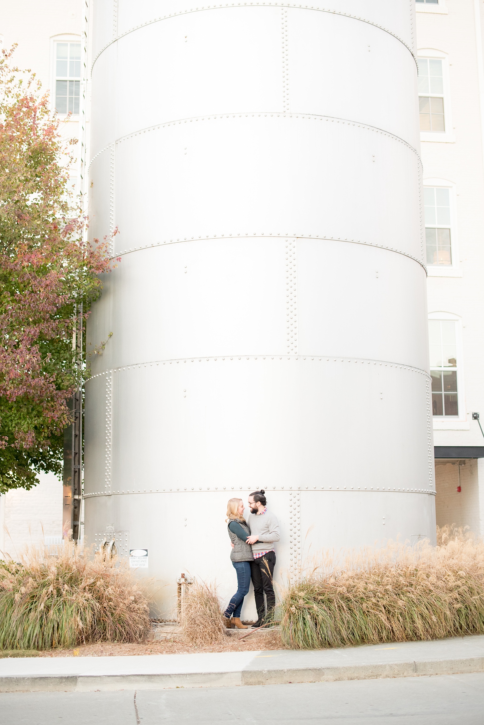 Mikkel Paige Photography photos of a Durham engagement session in downtown Durham. The bride and groom got cozy at American Tobacco Campus in this picture amongst the grasses.