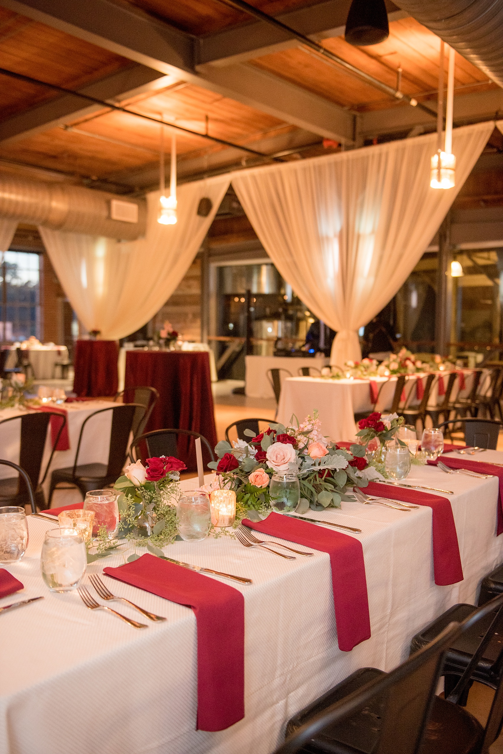 Mikkel Paige Photography photo of a wedding at The Rickhouse, NC. A picture of the rectangular and round mixed tables with burgundy linens and fall flowers and candlelight.