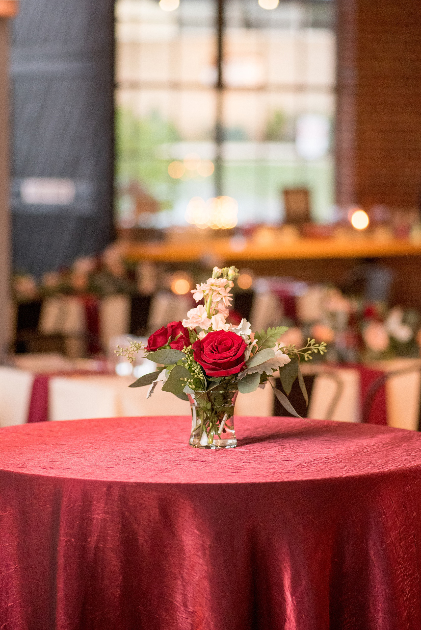 Mikkel Paige Photography photo of a wedding at The Rickhouse, NC. A picture of the rectangular and round mixed tables with burgundy linens and fall flowers and candlelight.