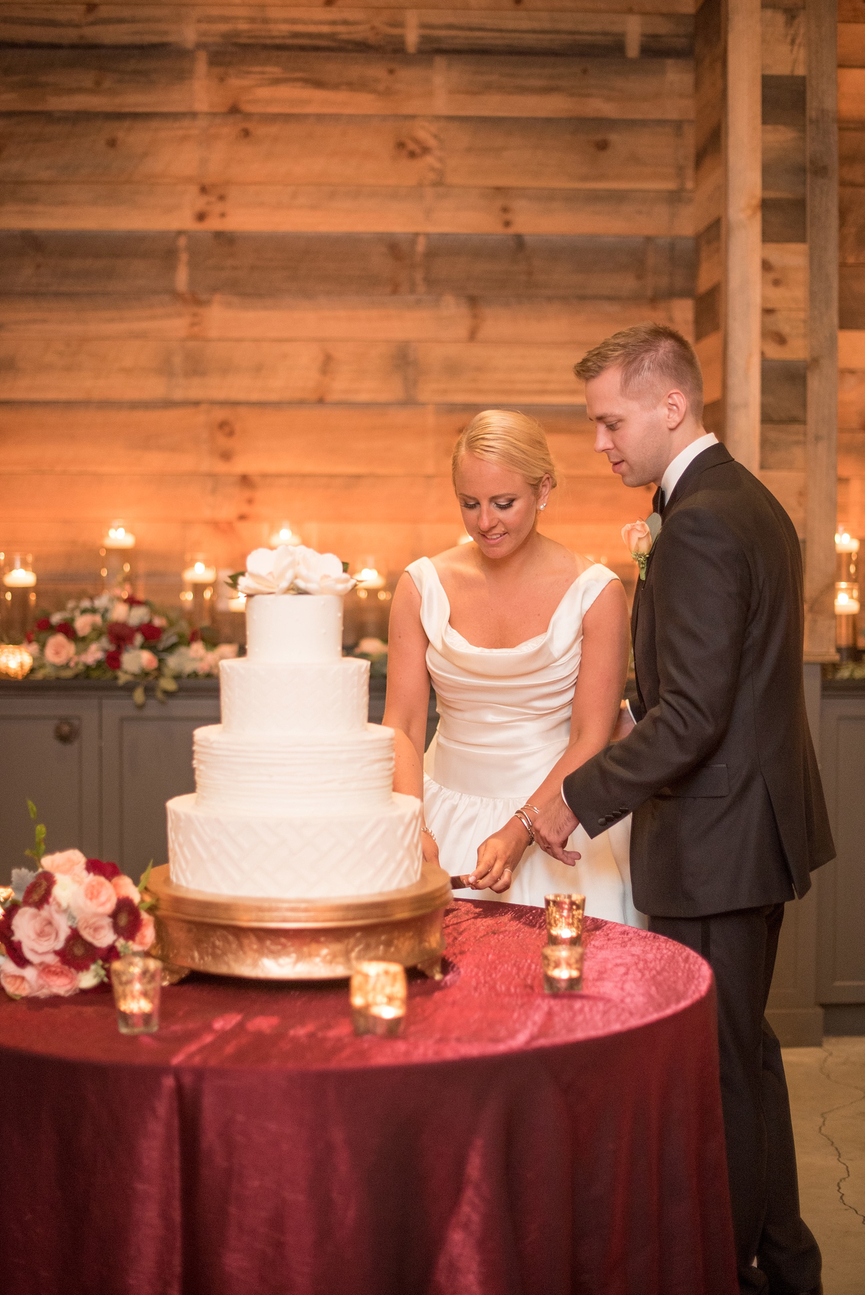 Mikkel Paige Photography photo of a wedding at The Rickhouse, NC. A picture of the bride and groom cutting their white tiered fondant wedding cake topped with gumpaste magnolia sugar flowers.