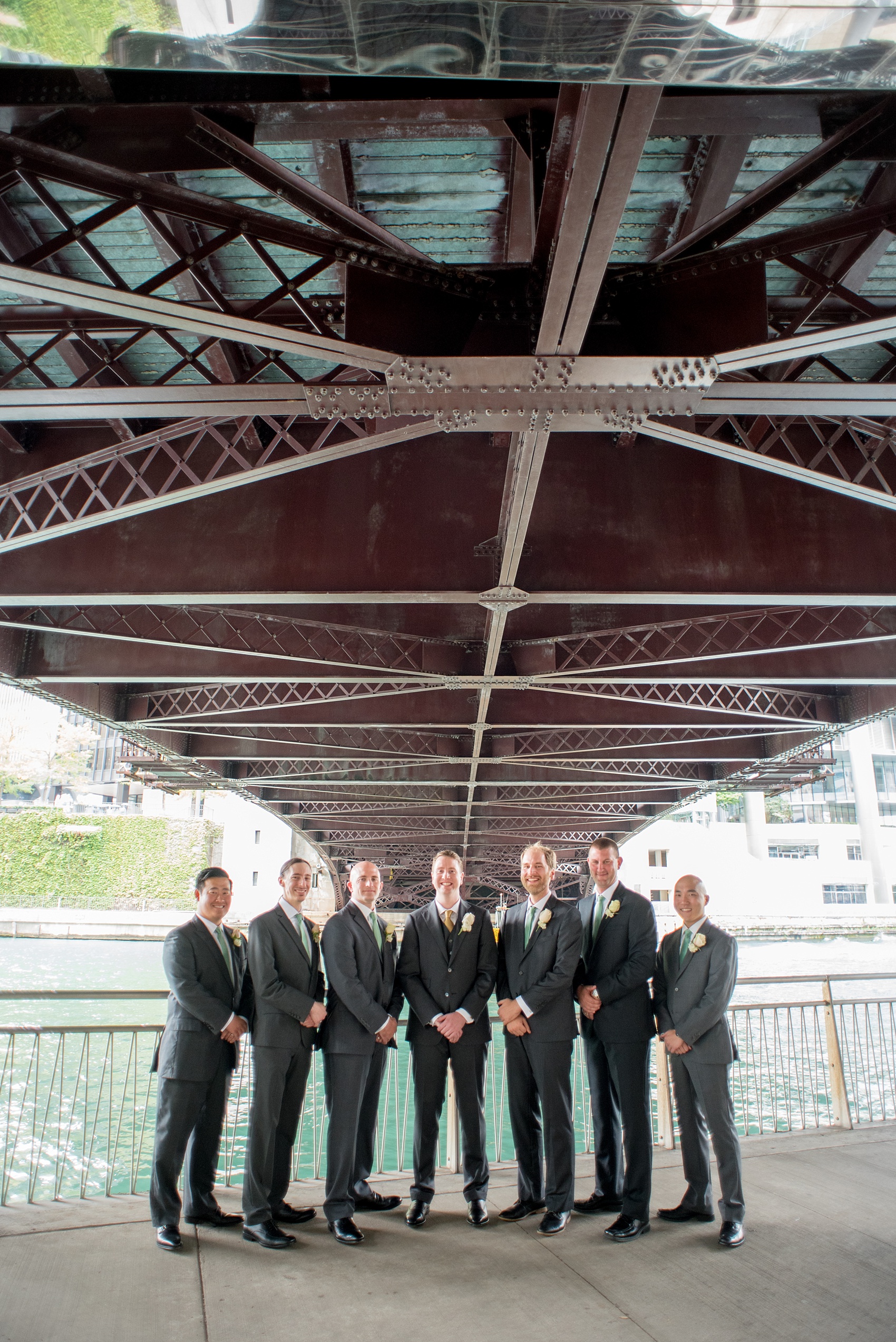 Mikkel Paige Photography photos of a wedding in downtown Chicago at The Rookery. The groomsmen in a unique, iconic photo under a Riverwalk bridge in grey suits with mint green ties.