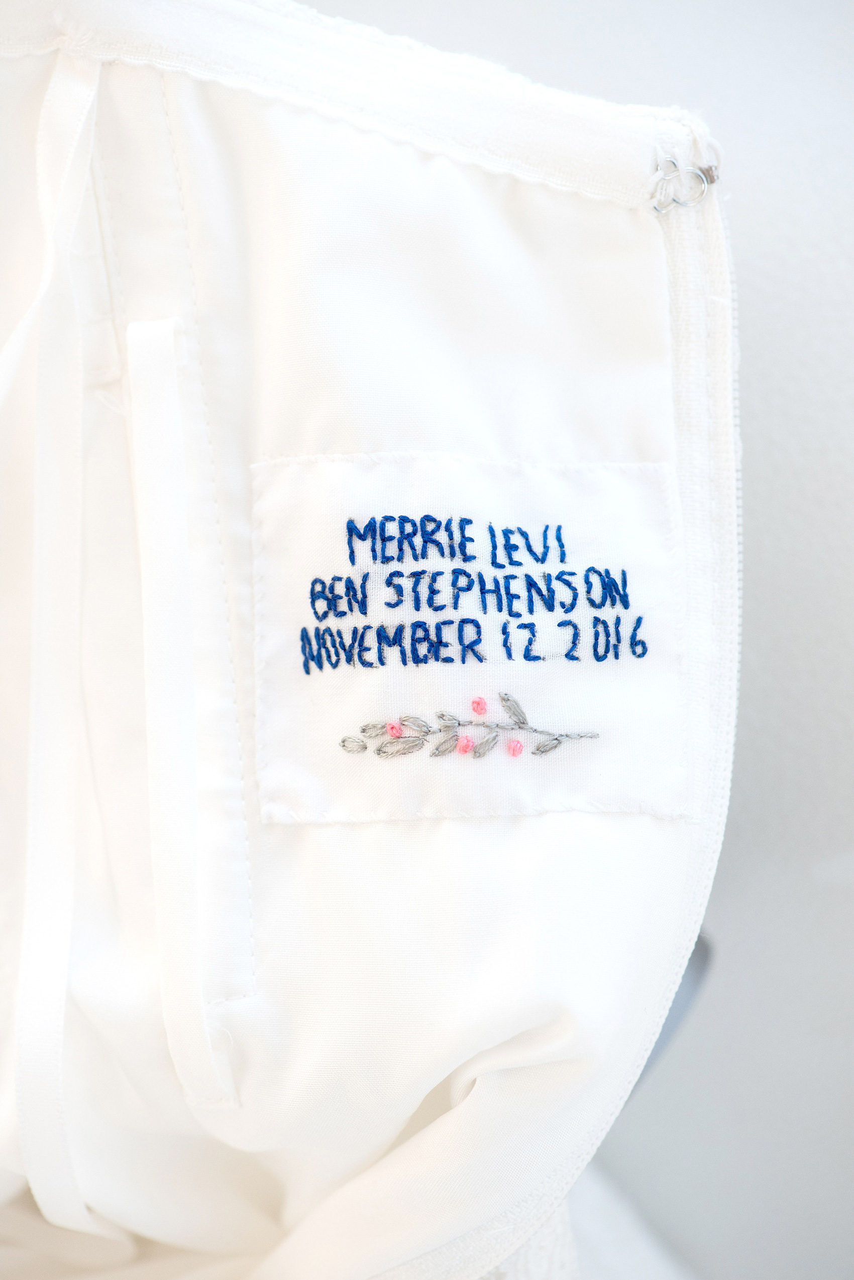 Mikkel Paige Photography photos from a wedding at The Glass Box and Stockroom at 230 in Raleigh. A detail image of the custom embroidered tag the bride's mother created for her daughter's wedding gown with the couple's date and names on it.
