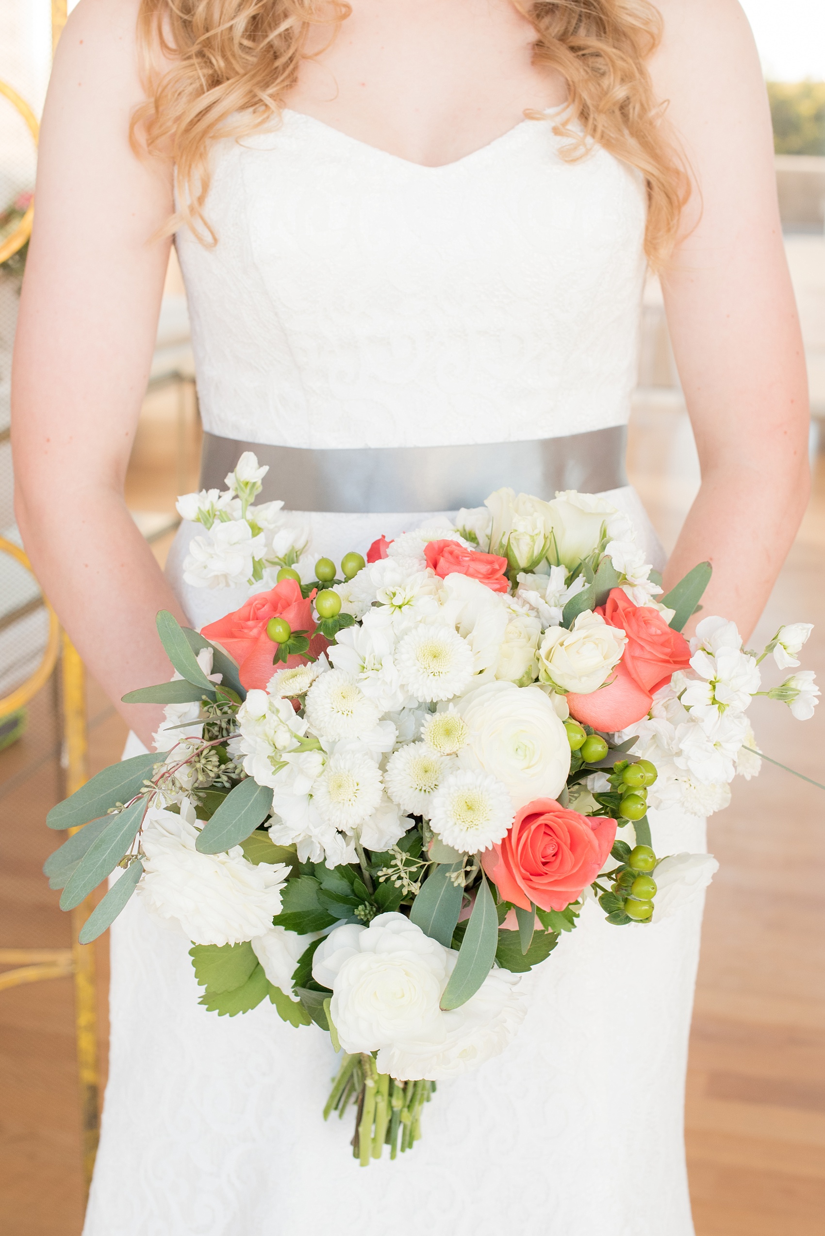 Mikkel Paige Photography photos from a wedding at The Glass Box and Stockroom at 230 in Raleigh. A picture of the bride in her lace strapless gown with grey belt and coral and white bouquet.