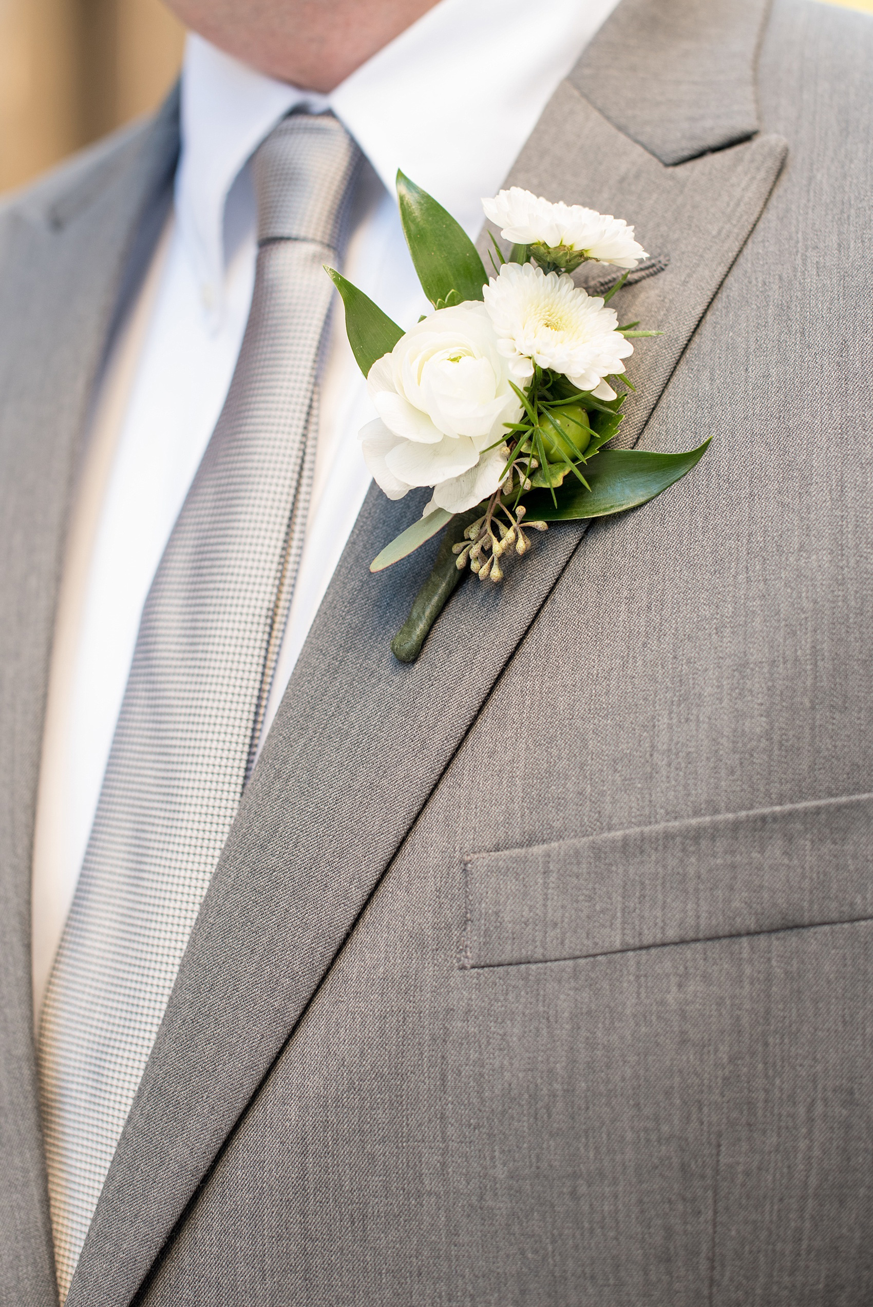 Mikkel Paige Photography photos from a wedding at The Glass Box and Stockroom at 230 in Raleigh. A picture of the groom's grey suit and tie with white boutonniere.