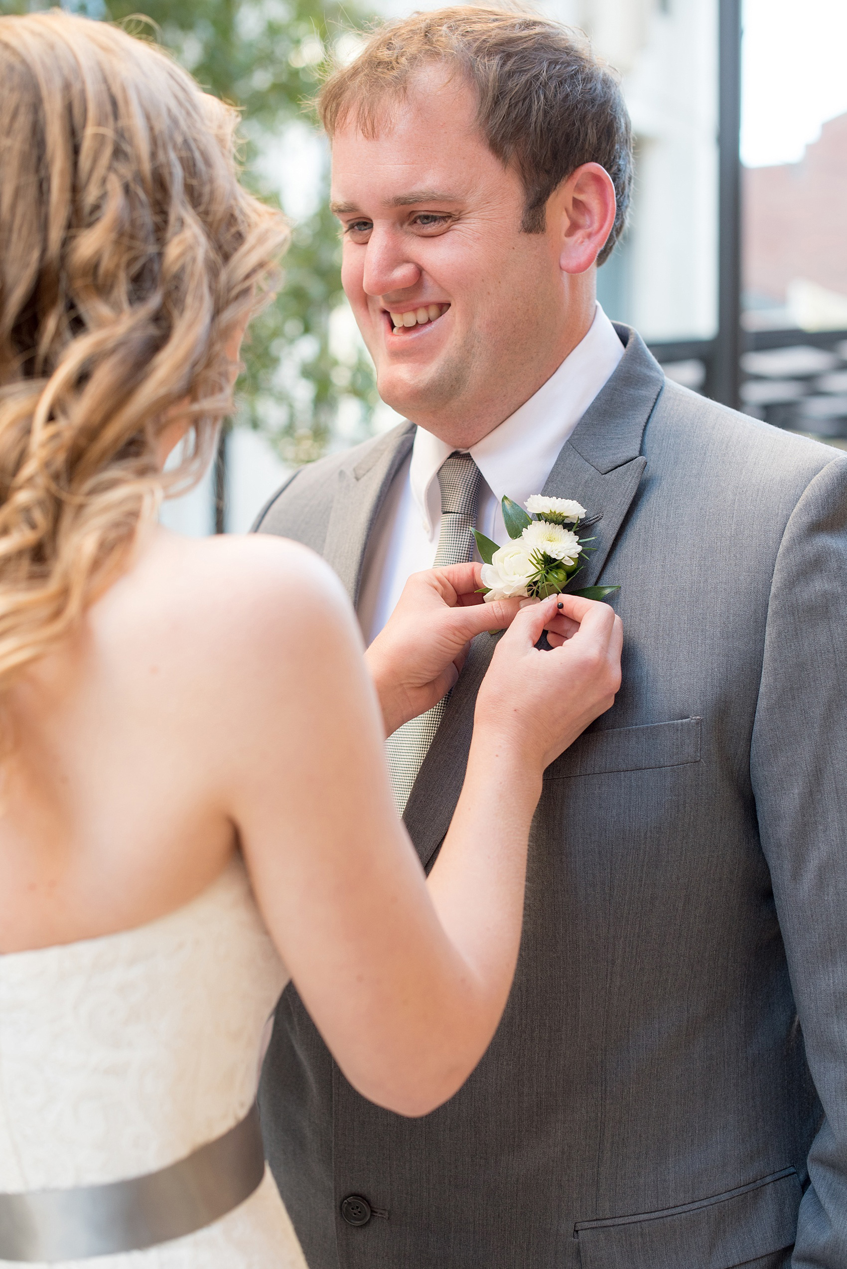 Mikkel Paige Photography photos from a wedding at The Stockroom at 230. A picture of the bride and groom in downtown Raleigh with the bride pinning on the groom's boutonniere for a wedding day tradition.