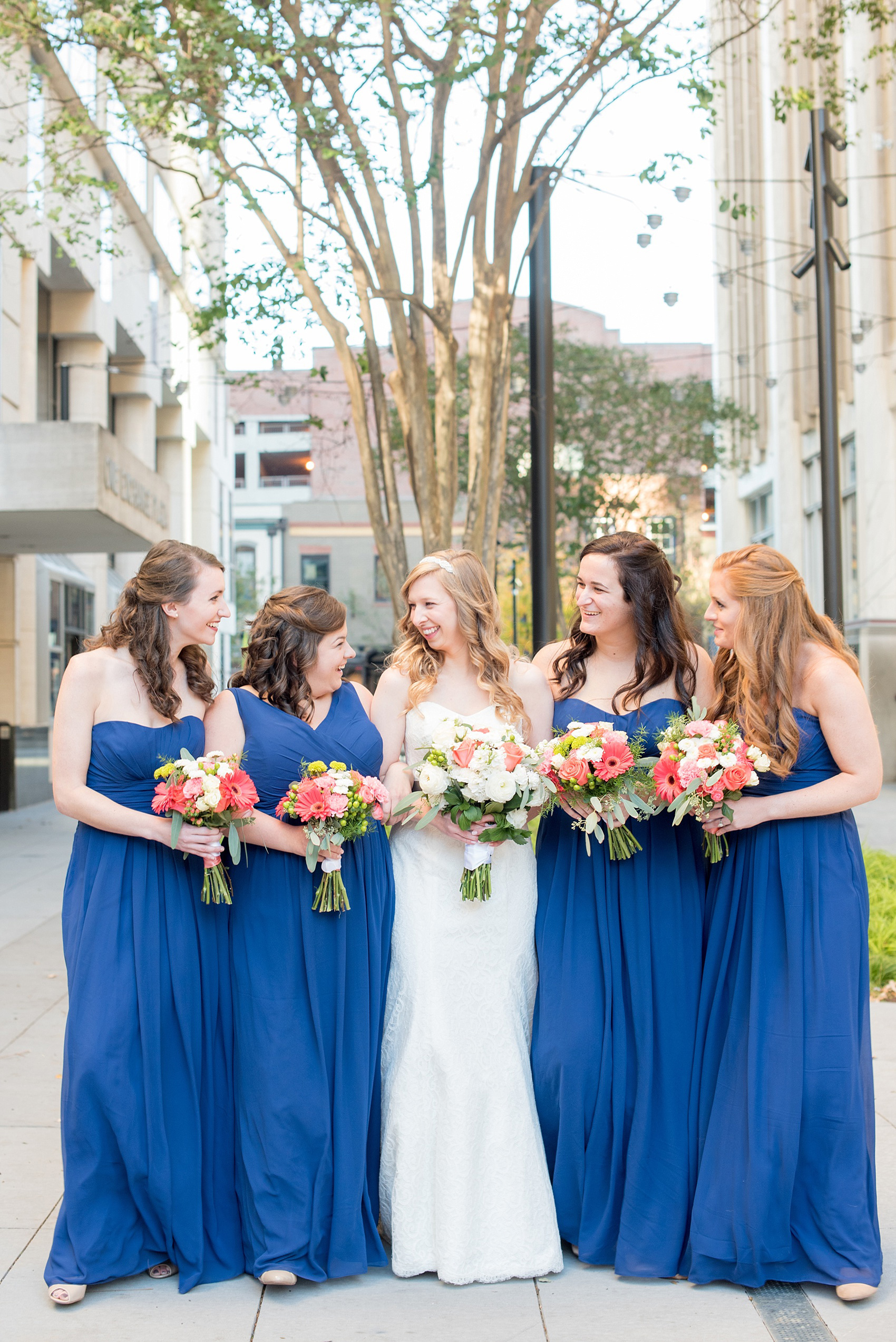 Mikkel Paige Photography photos from a wedding at The Stockroom at 230. A picture of the bride and her bridesmaids in cobalt blue in downtown Raleigh with coral and white bouquets.