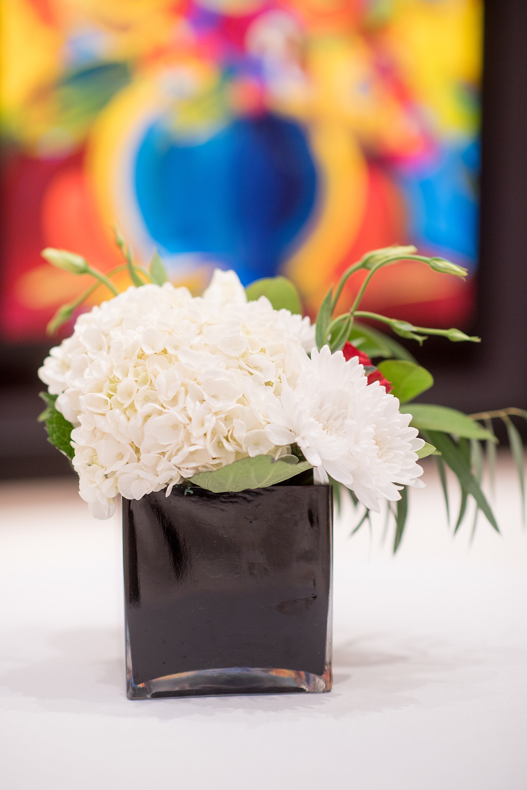 Mikkel Paige Photography photos from The Stockroom at 230 in downtown Raleigh. A picture of the white floral centerpiece in black vase for cocktail hour in the Mahler Building with Peter Max art.