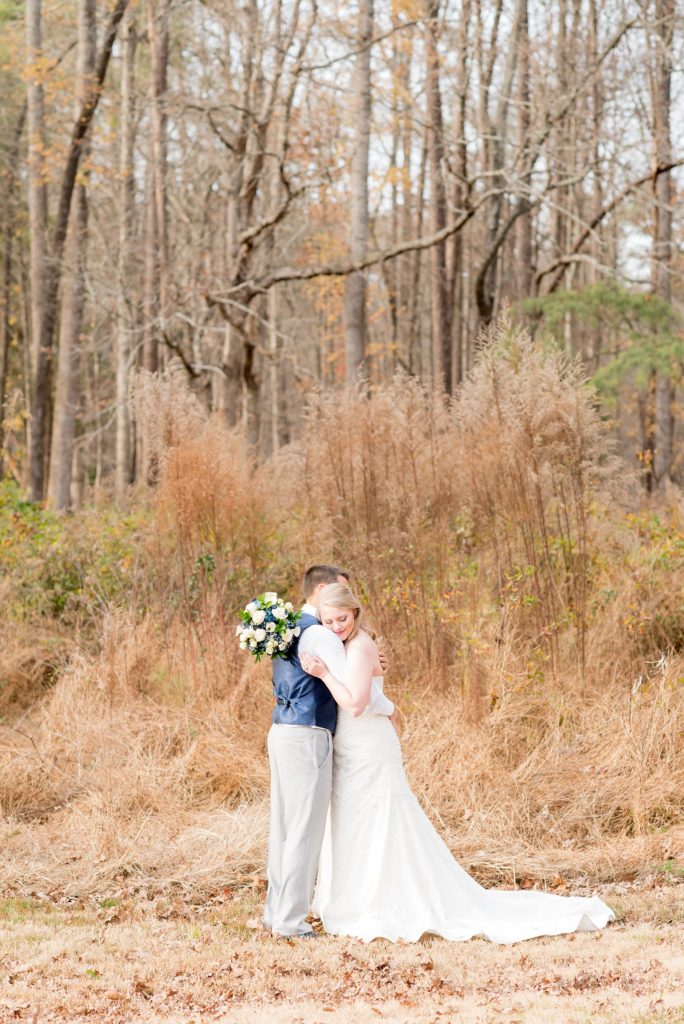 Mikkel Paige Photography photos of a wedding at The Barn at Valahalla in Chapel Hill, NC. The bride hugs her groom in this picture in front of tall autumn colored grasses and evergreen trees.