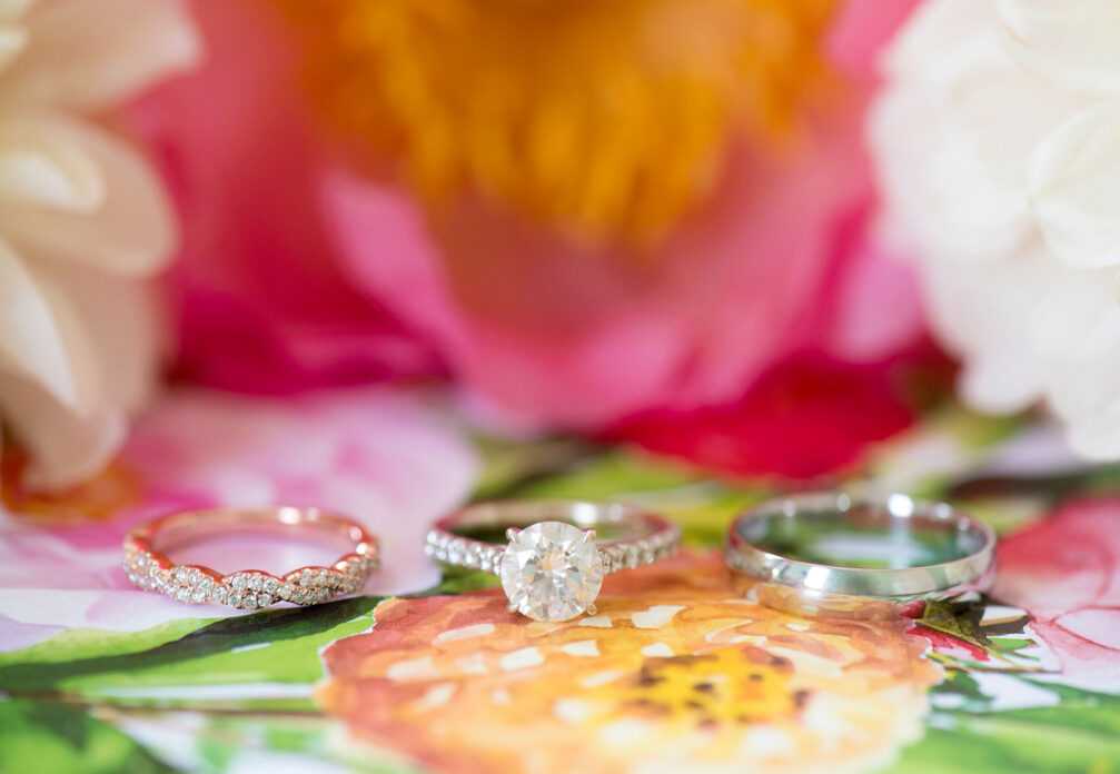 Mikkel Paige Photography photos of a wedding at Merrimon-Wynne House in downtown Raleigh. Detail picture of the wedding bands in white and rose gold on the couple's floral invitation liner.