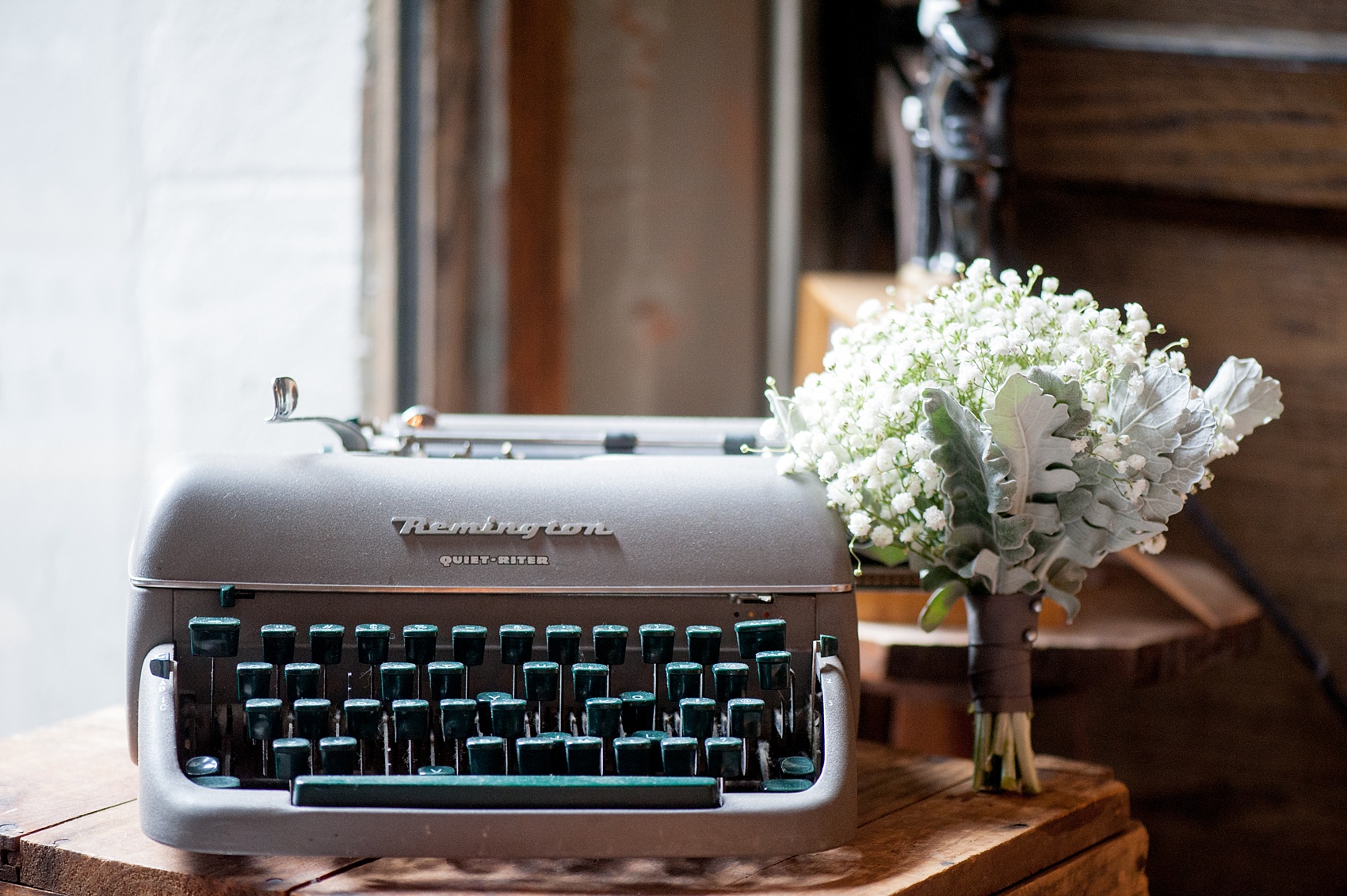 Mikkel Paige Photography Brooklyn Winery wedding photos. Detail picture of a bridesmaids bouquet of Dusty Miller and Baby's Breath flowers tied with grey ribbon near a vintage typewriter.