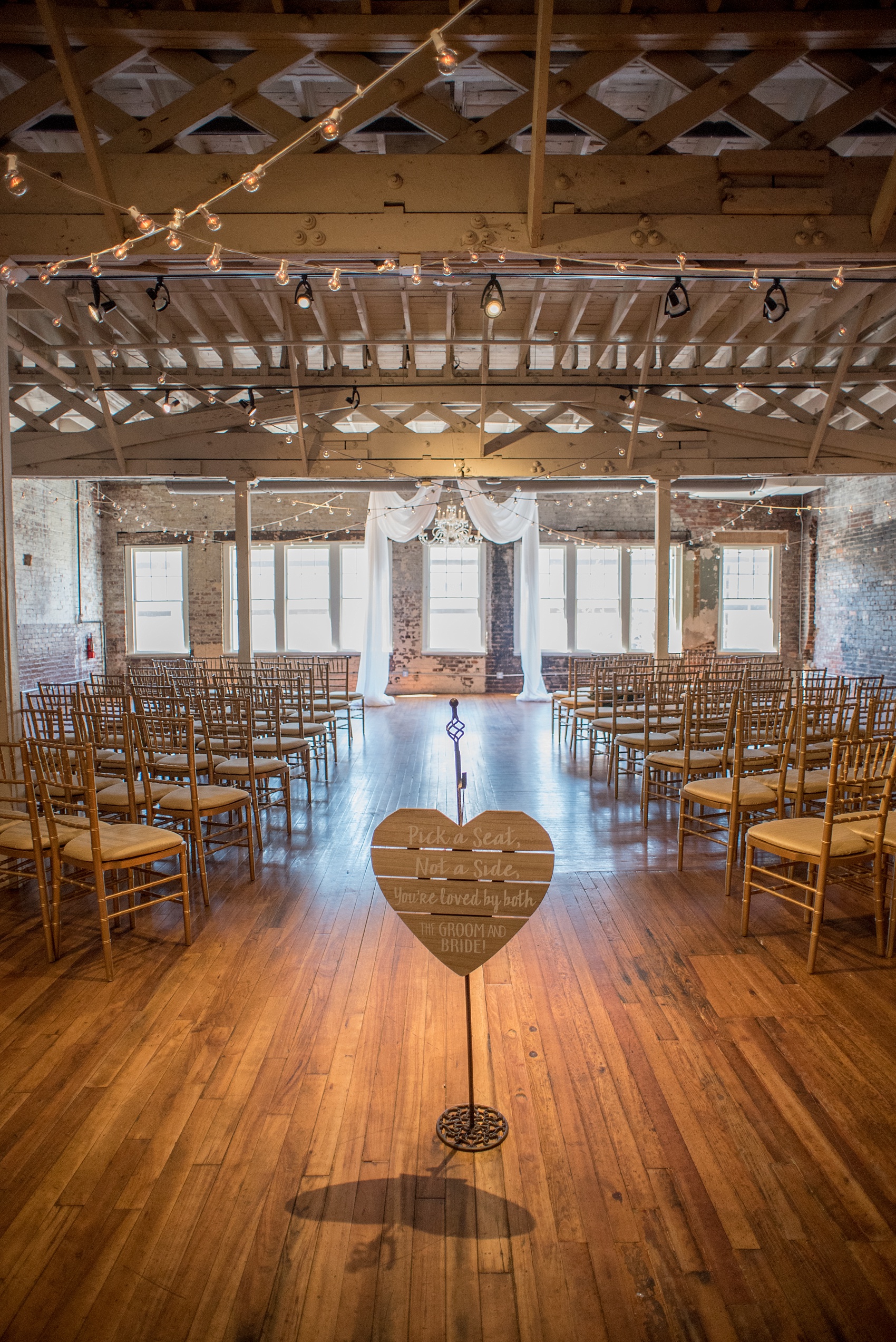 Mikkel Paige Photography photos of a small wedding at The Stockroom at 230 in downtown Raleigh, North Carolina. Image of the ceremony setup with chandelier, side seating signage and drapery at the alter. 