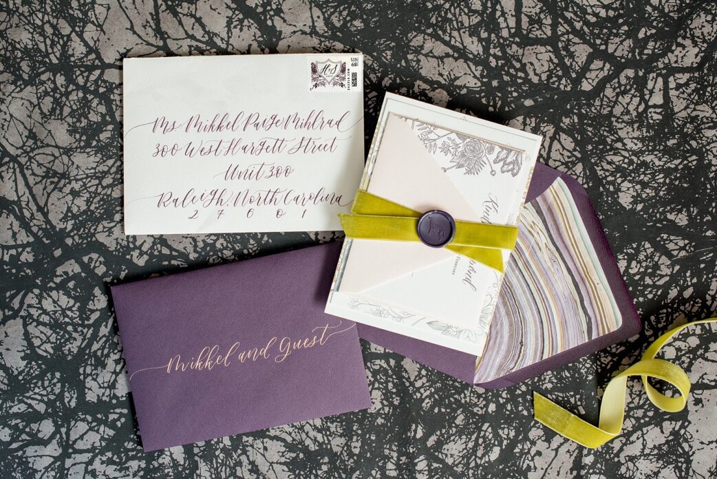 Mikkel Paige Photography image of a wedding invitation suite in purple, grey and copper by One and Only Paper. Calligraphy by Quietude Co in Raleigh, NC. Velvet yellow-green chartreuse ribbon and custom wax seals with the couples greyhound dog were included. The envelope liner was agate gem marble inspired.