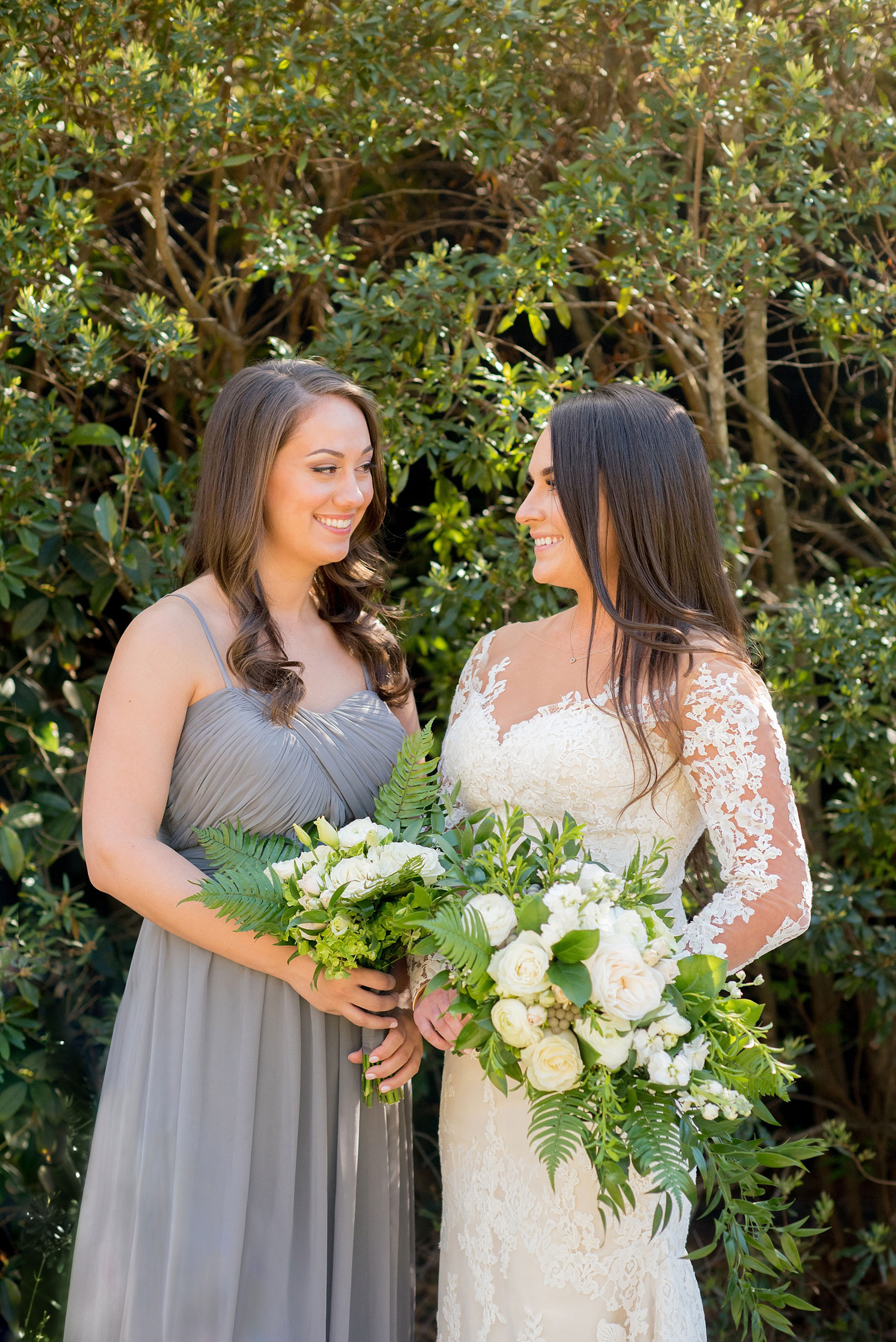 The Sutherland Wedding Photos by Mikkel Paige Photography. A picture of the Maid of Honor bridesmaid in grey chiffon gown and bride in lace Pronovias with green and white bouquet by Eclectic Sage. Planning by A Southern Soiree.