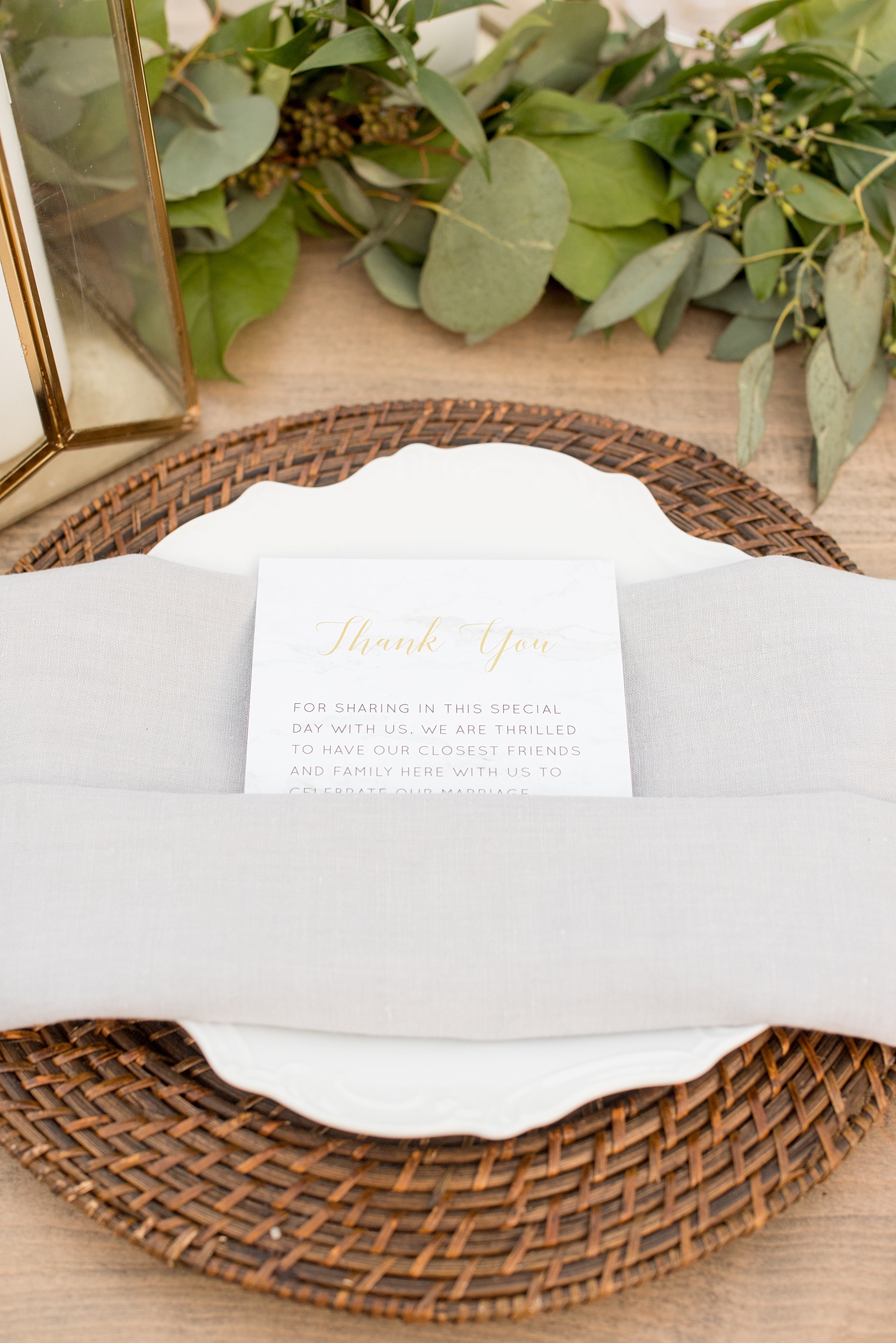 The Sutherland Wedding Photos by Mikkel Paige Photography. Grey and white farm tables by Cottage Luxe, with eucalyptus leaf garland and wooden chargers. A custom thank you note from the couple rests on top of the plates. Planning by A Southern Soiree.