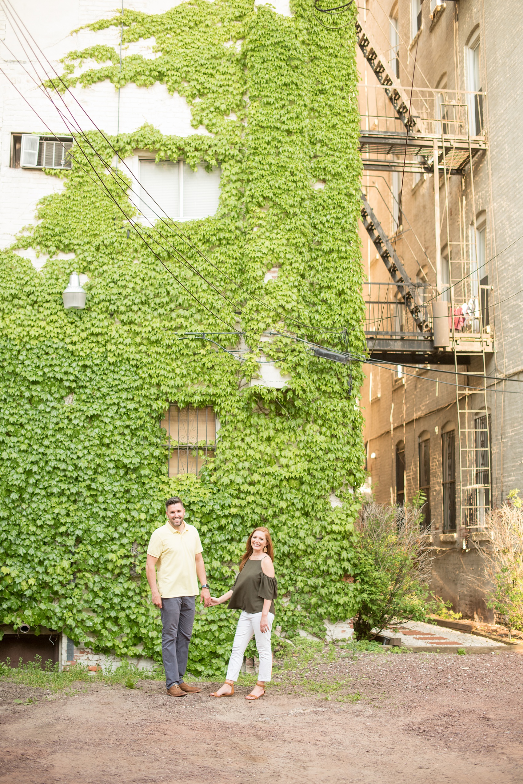 Spring Hoboken Engagement Photos by Mikkel Paige Photography. Picture of the couple in an urban city setting in front of a green ivy wall.