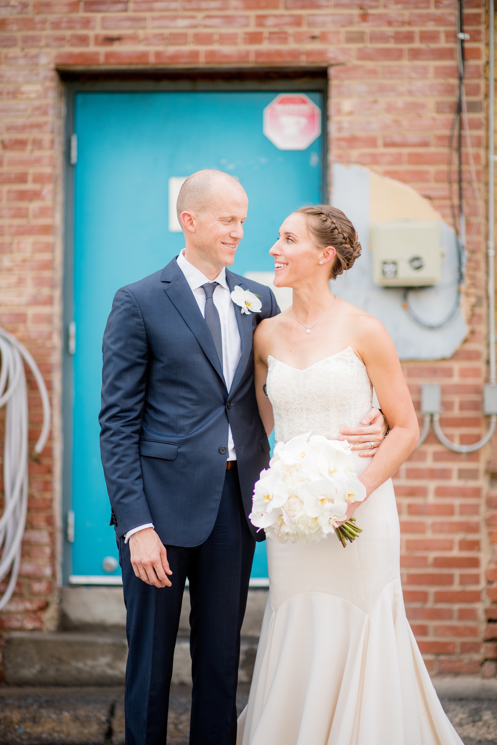 The Cookery Durham wedding photos by Mikkel Paige Photography. Picture of the bride and groom with white orchid flowers in front of a colorful door and brick wall in an urban setting.
