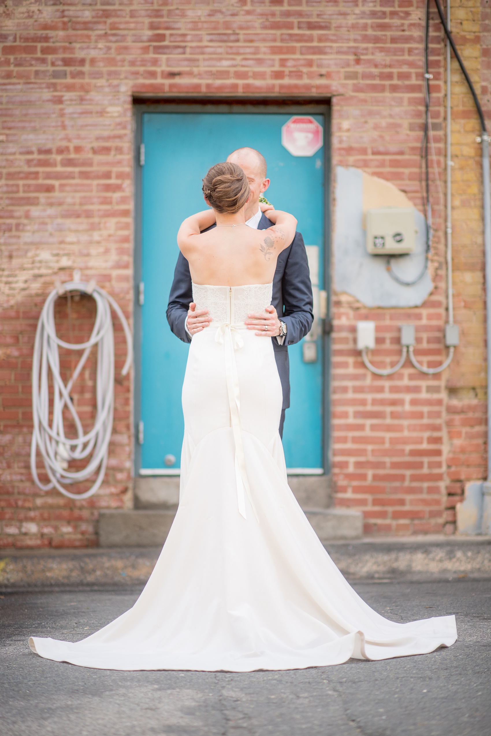 The Cookery Durham wedding photos by Mikkel Paige Photography. Picture of the bride's gown train with arms around her groom in front of a colorful door and brick wall in an urban setting.