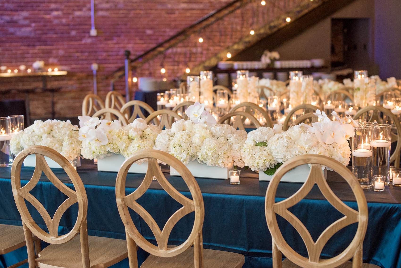 The Cookery Durham wedding photos by Mikkel Paige Photography. Picture of the teal and neutral colored wood palette by Erin McLean Events. Candlelight and rectangular tables were the seating for guests in this charming venue. Flower boxes by Tre Bella included hydrangeas, peonies and white orchids.