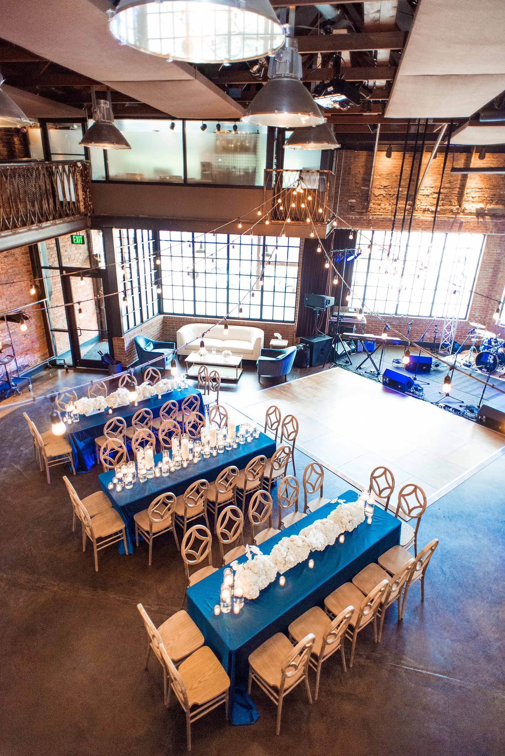 The Cookery Durham wedding photos by Mikkel Paige Photography. Picture of an aerial view of the room with teal and neutral colored wood palette by Erin McLean Events. Candlelight and rectangular tables were the seating for guests in this charming venue. Flower boxes by Tre Bella included hydrangeas, peonies and white orchids.