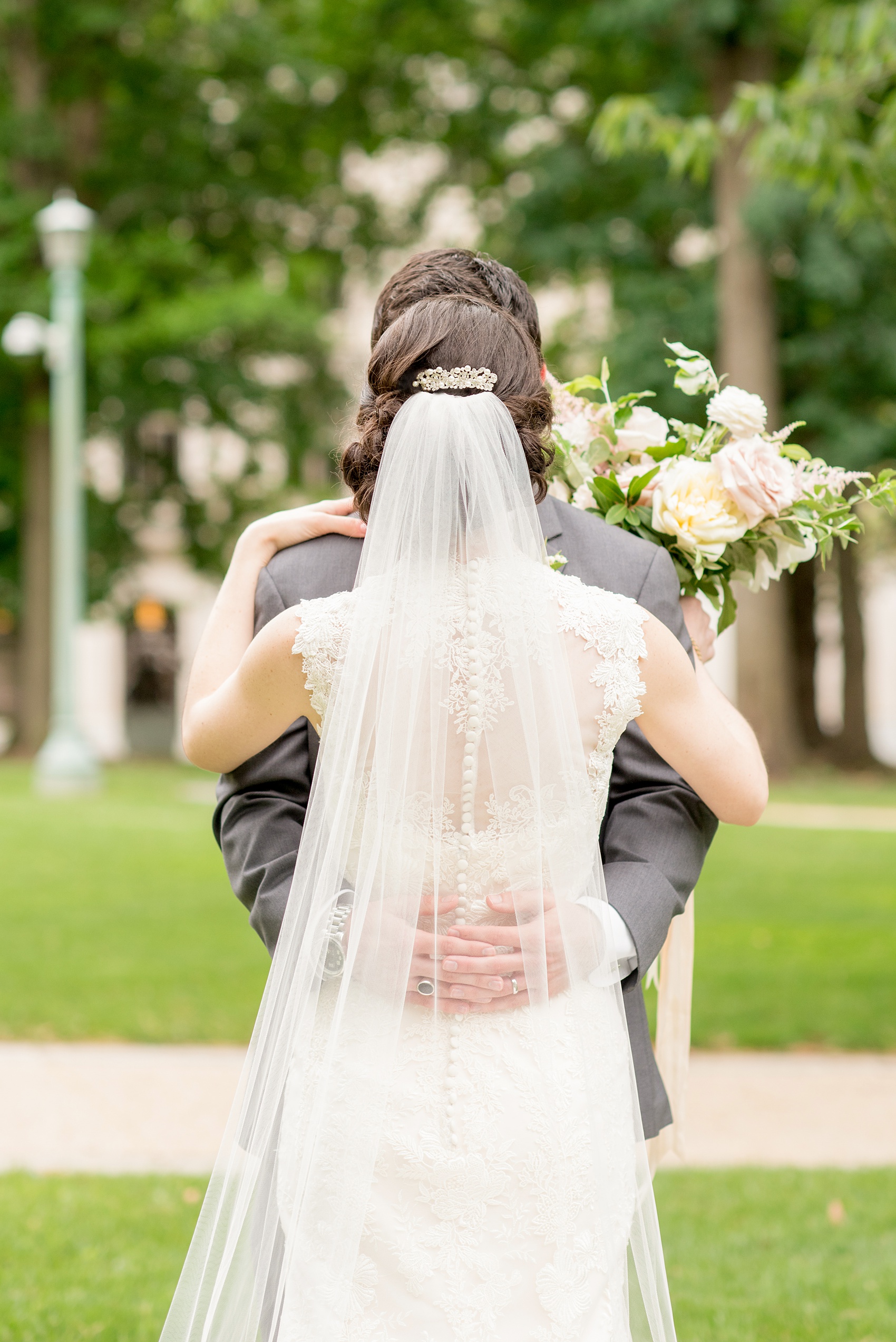 Wedding photos by Mikkel Paige Photography. Picture of the bride and groom at the Raleigh capitol building during a spring day. Her veil cascades over her lace gown.