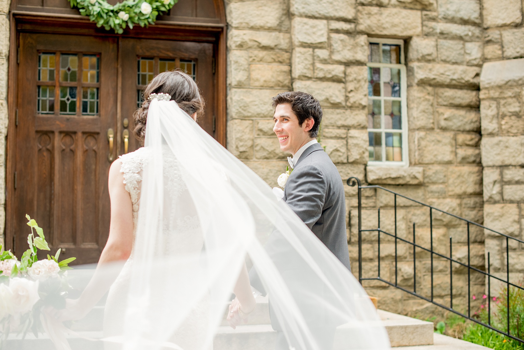 Wedding photos by Mikkel Paige Photography at Sacred Heart Cathedral in downtown Raleigh. Picture of the bride and groom entering the church as her veil blows in the breeze.