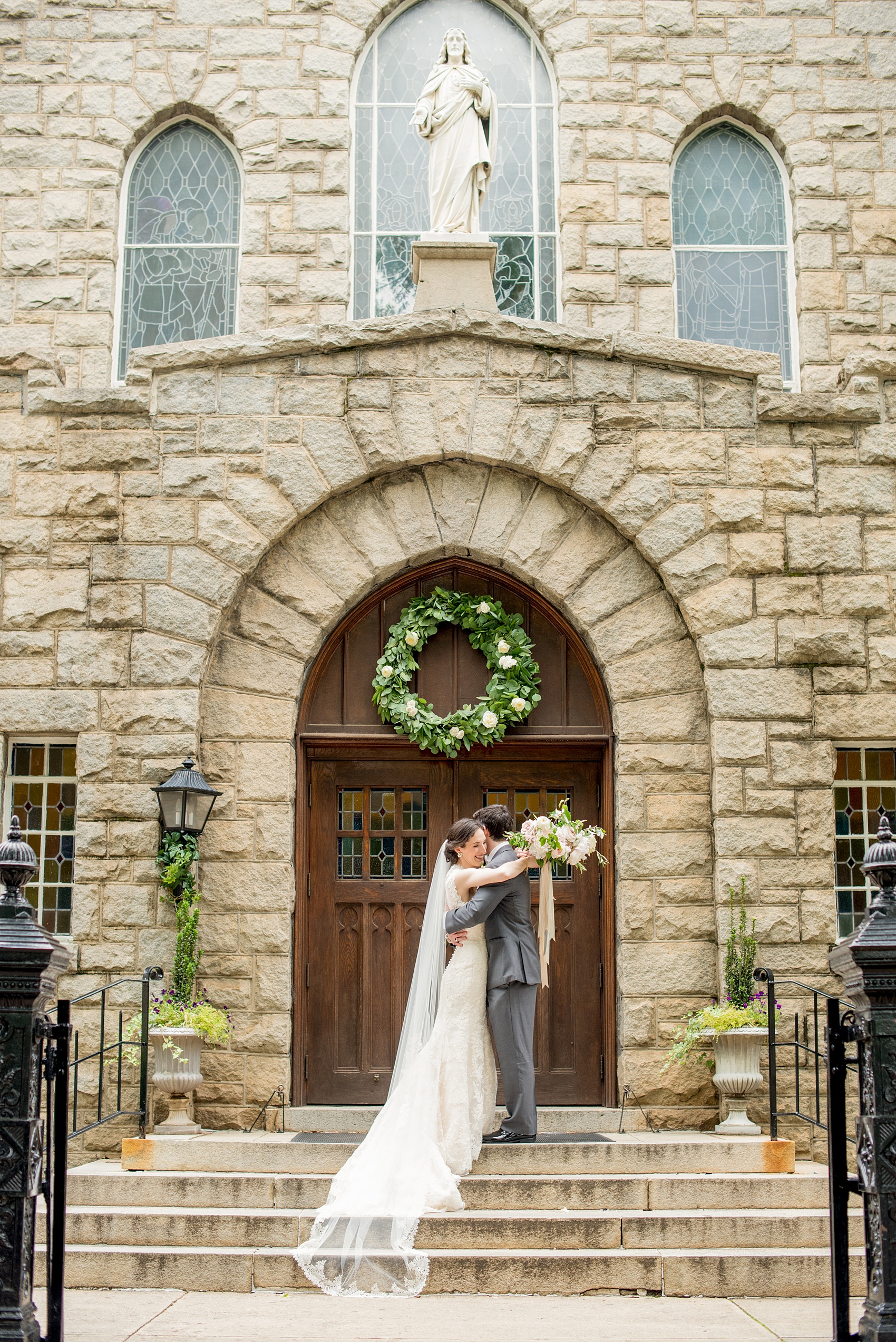 Wedding photos by Mikkel Paige Photography at Sacred Heart Cathedral in downtown Raleigh of the bride and groom as newlyweds in front of the stone church. Wreath by Meristem Floral.