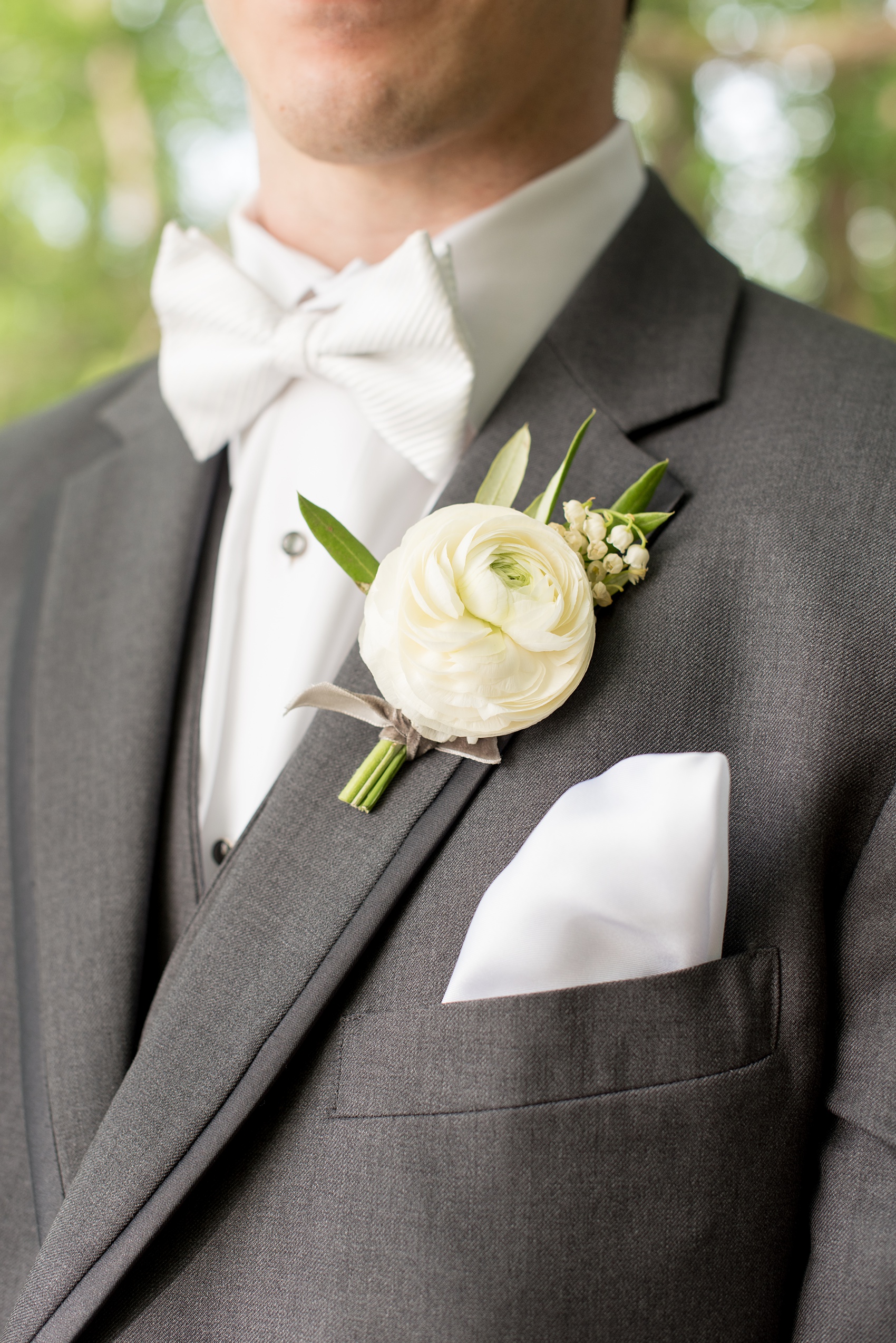 Pavilion at Angus Barn wedding photos by Mikkel Paige Photography. Detail picture of the groom's ranunculus and white lily-of-the-valley boutonniere tied with grey velvet ribbon by Meristem Floral.