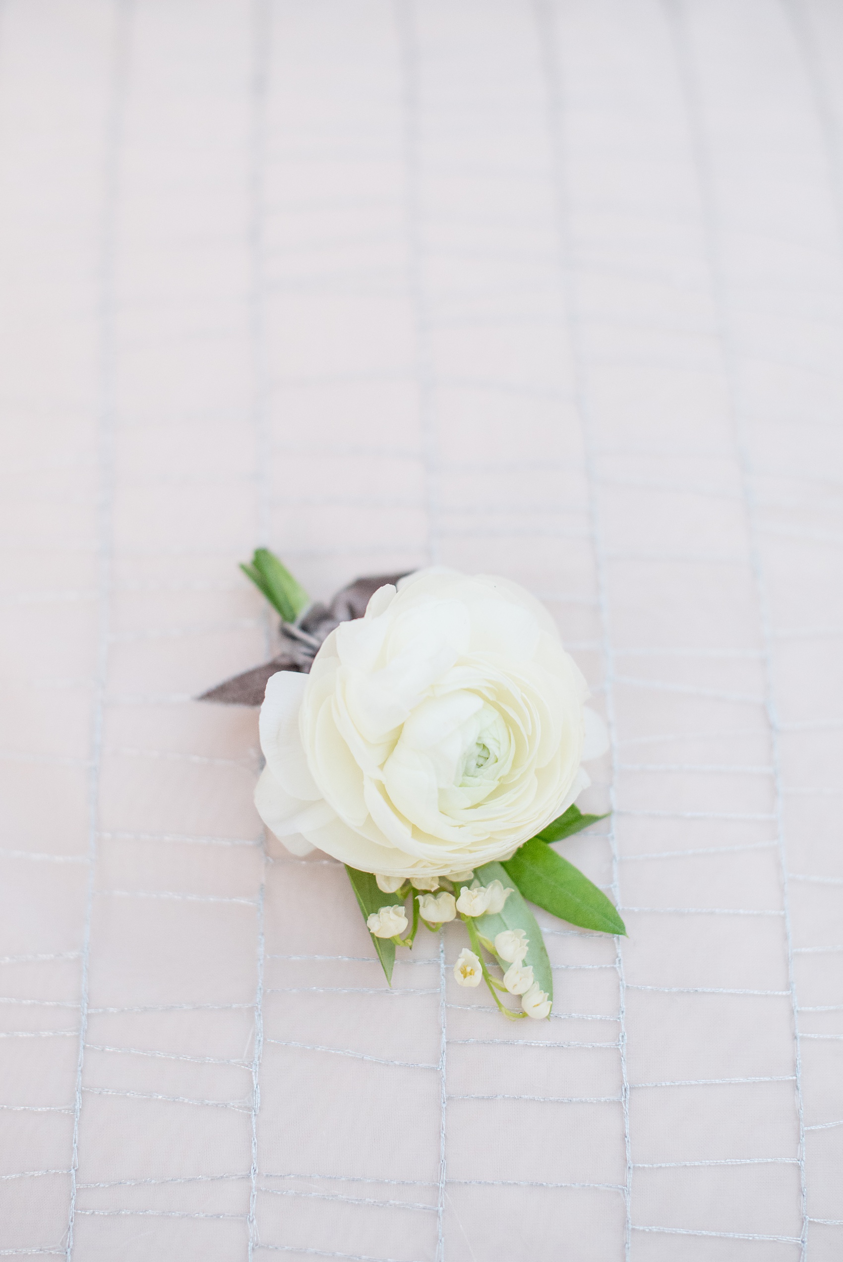 Pavilion at Angus Barn wedding photos by Mikkel Paige Photography. Picture of a boutonniere with a white ranunculus and Lily of the Valley by Meristem Floral. Tied with grey velvet ribbon. 