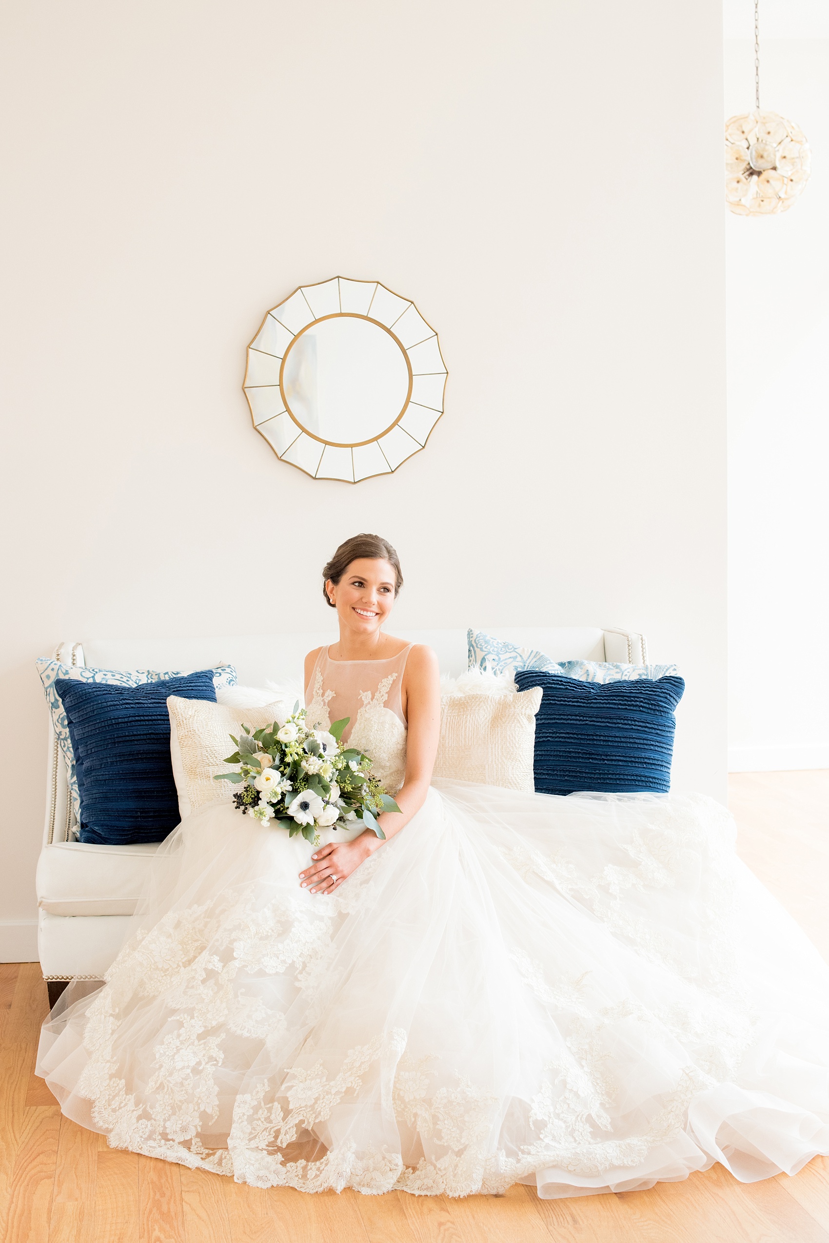 The Glass Box Raleigh wedding photos by Mikkel Paige Photography. Image of a bride in a white gown on a white couch with blue throw pillows.