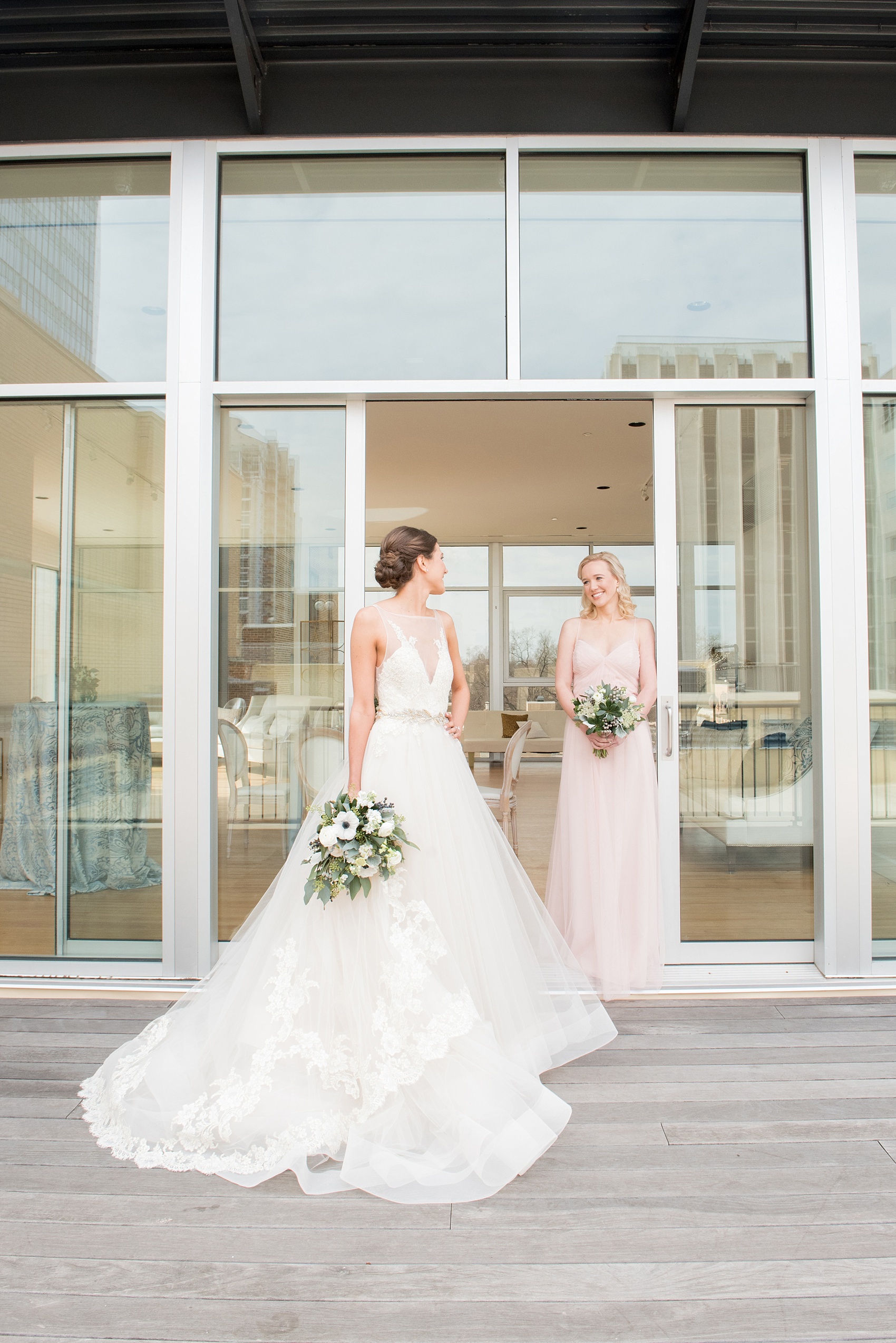 The Glass Box Raleigh wedding photos by Mikkel Paige Photography. Picture of the bride in a Lazaro gown in this modern downtown venue rooftop. The bridesmaid wore a pink Hayley Paige occasion gown.