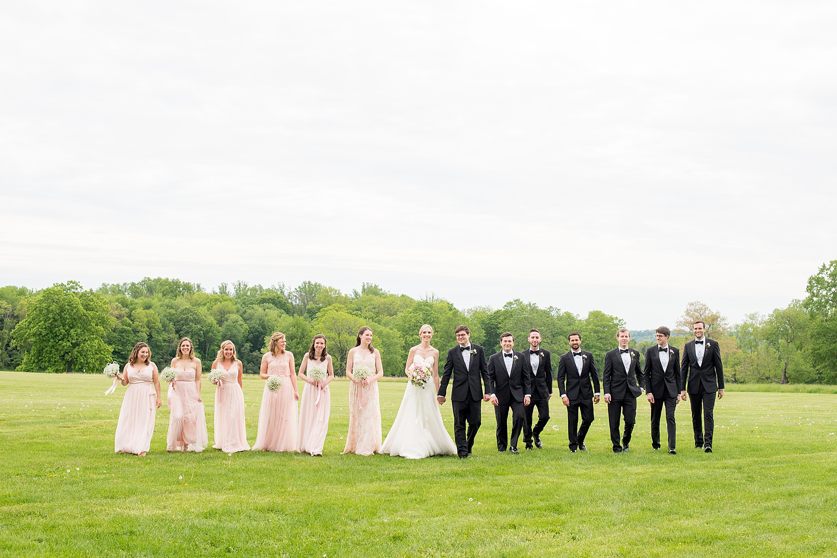 Waveny House wedding photos in Connecticut by Mikkel Paige Photography. Picture of the bride in a strapless gown with her bridesmaids in pink dresses, and maid of honor in a pink floral pattern gown. Bridesmaids held Baby's Breath bouquets. The groomsmen wore classic black tuxedos.