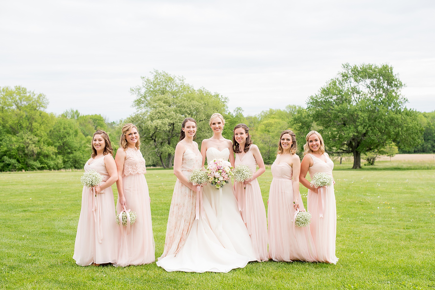 Waveny House wedding photos in Connecticut by Mikkel Paige Photography. Creative picture of the bride in a strapless gown with her bridesmaids in pink dresses, and maid of honor in a pink floral pattern gown. Bridesmaids held Baby's Breath bouquets.
