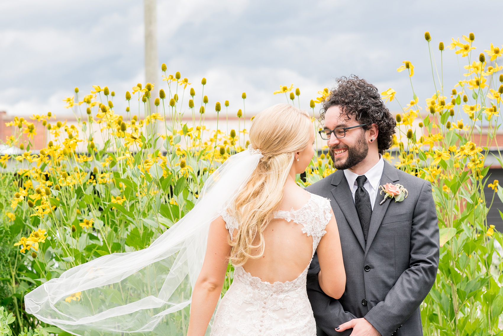 Mikkel Paige Photography photos from a wedding in Durham, North Carolina. Picture of the bride and groom with yellow flowers behind them and the bride's peek-a-boo back lace gown.