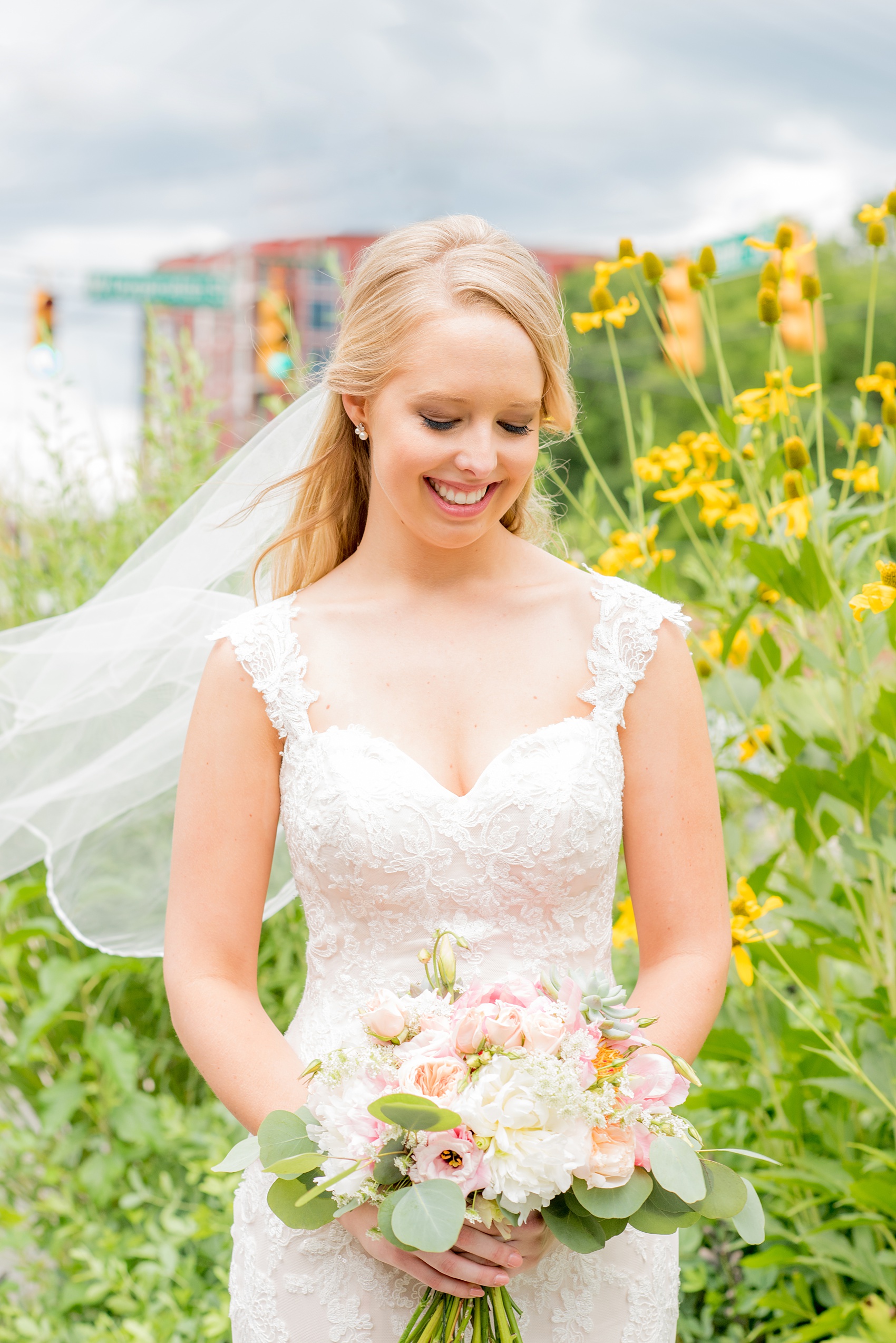 Mikkel Paige Photography photos from a wedding in Durham, North Carolina. Picture of the bride with yellow flowers behind her and veil blowing in the wind. She held a bouquet with peonies, succulents and eucalyptus.