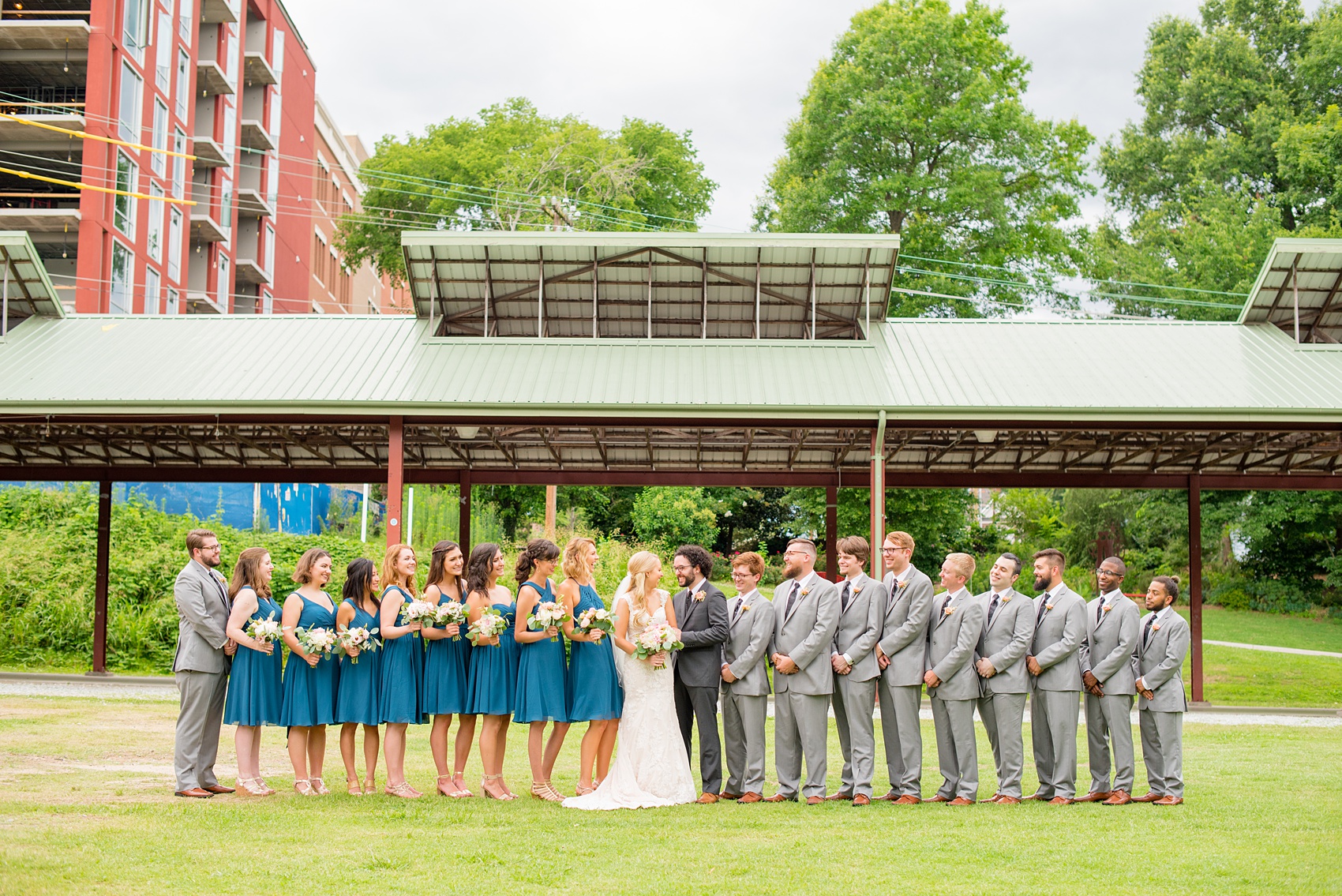 Mikkel Paige Photography photos from a wedding in Durham, North Carolina. Picture of the large wedding party - with the bridesmaids in teal and groomsmen in grey - in a picture in the park.