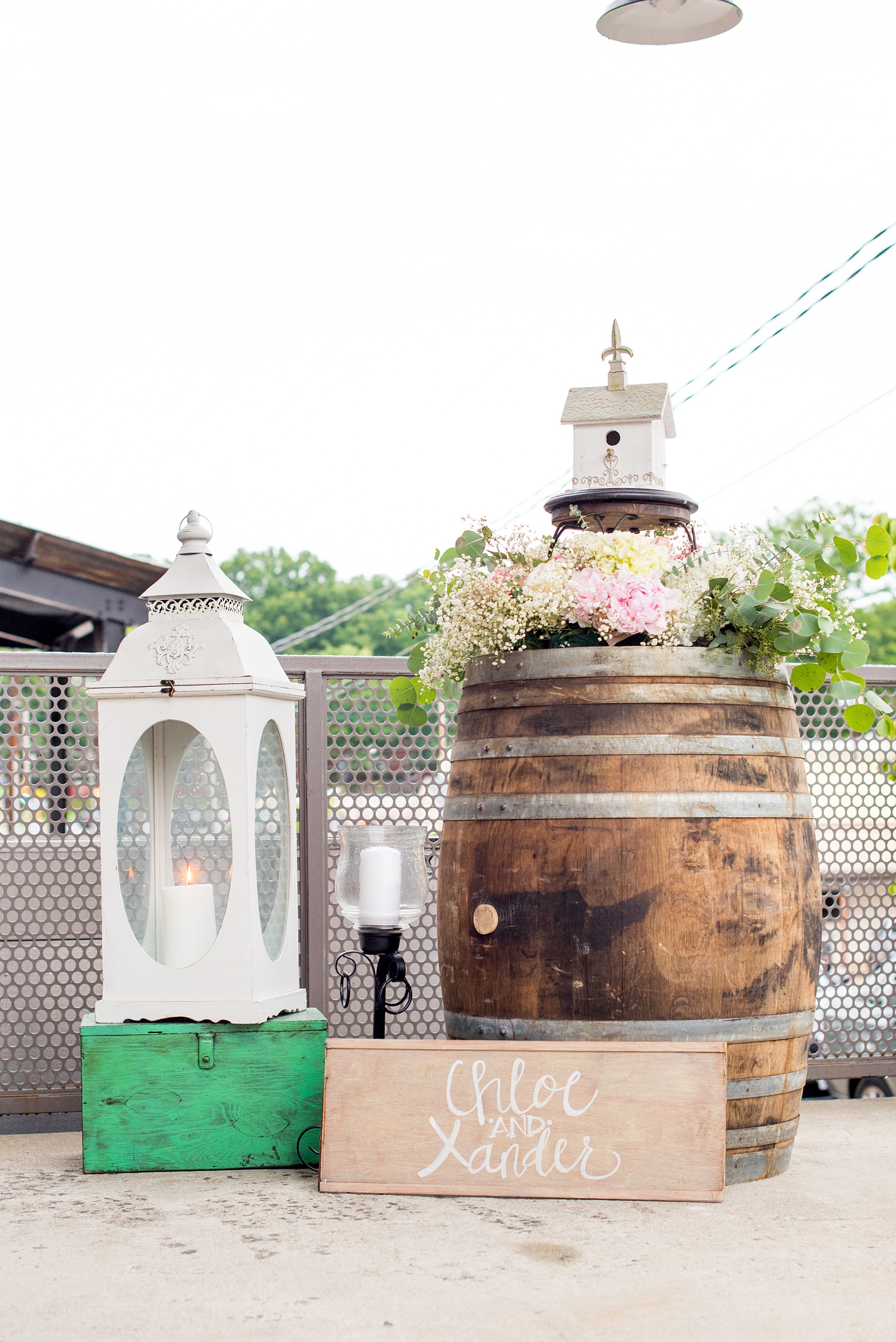 Mikkel Paige Photography photos from a wedding in Durham, North Carolina. Picture of the entrance to their wedding at The Rickhouse including flowers, a whiskey barrel, lantern and a birdhouse.
