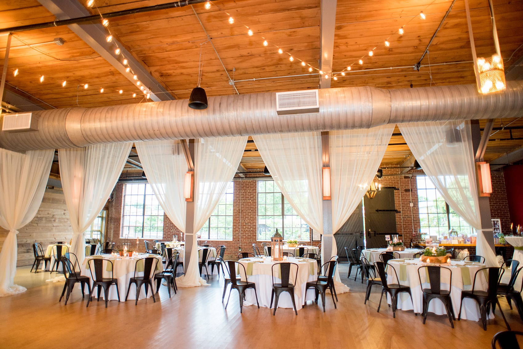 Mikkel Paige Photography photos from a wedding at The Rickhouse in Durham, North Carolina. Picture of the reception setup with metal chairs, draping and rustic lantern centerpieces.