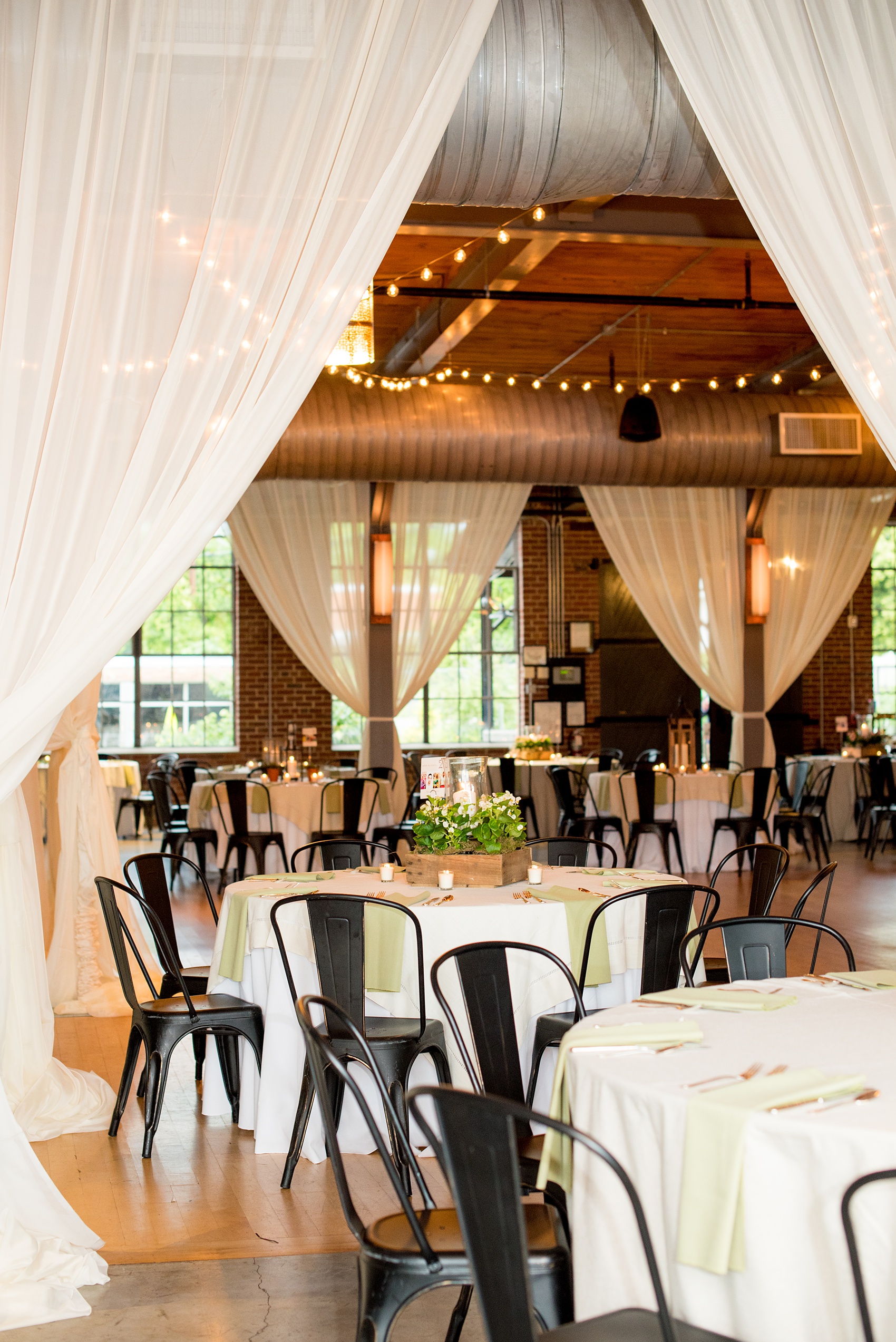 Mikkel Paige Photography photos from a wedding at The Rickhouse in Durham, North Carolina. Picture of the reception setup with metal chairs, draping and rustic lantern centerpieces.